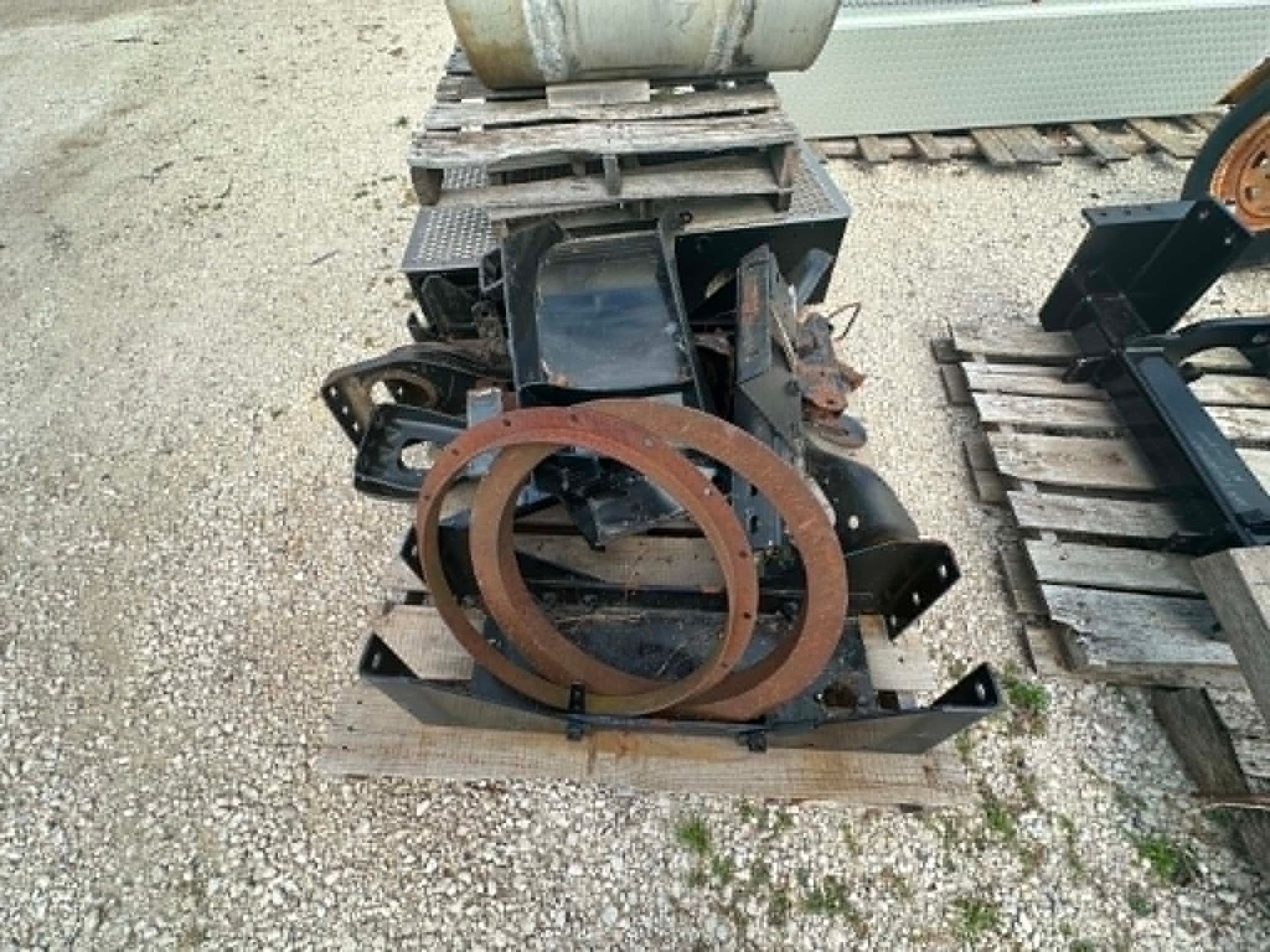 Rusty industrial machine part on a pallet outdoors on gravel, with a large circular ring in front.