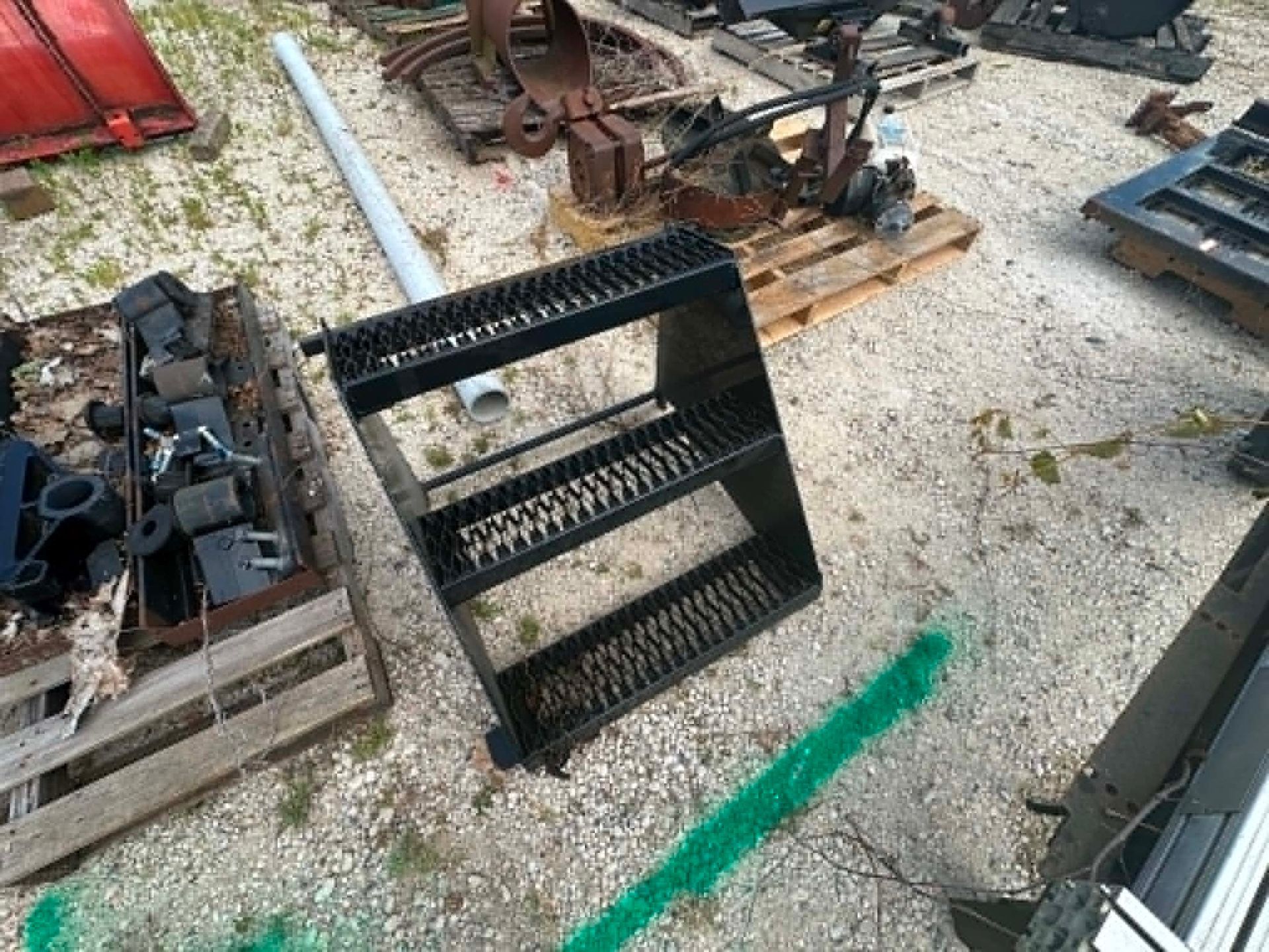 Black metal staircase in an outdoor scrapyard with scattered debris and machinery.