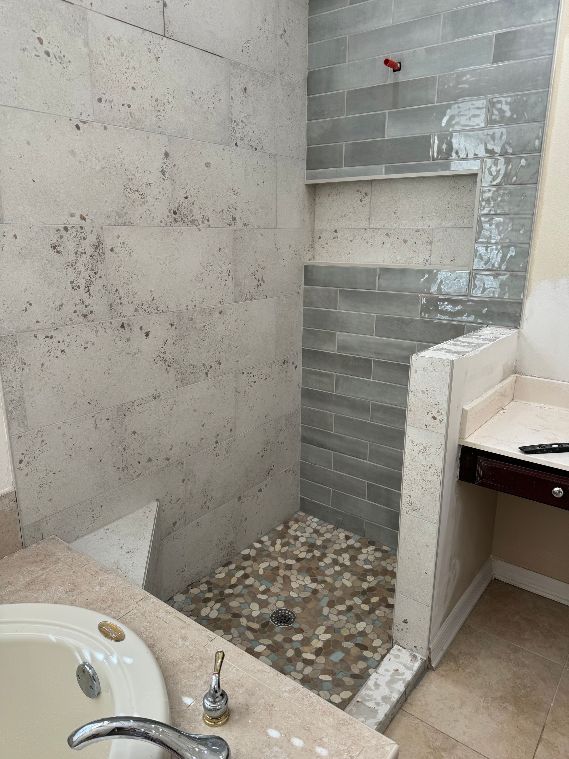 Partially tiled bathroom with a walk-in shower and sink counter in the foreground