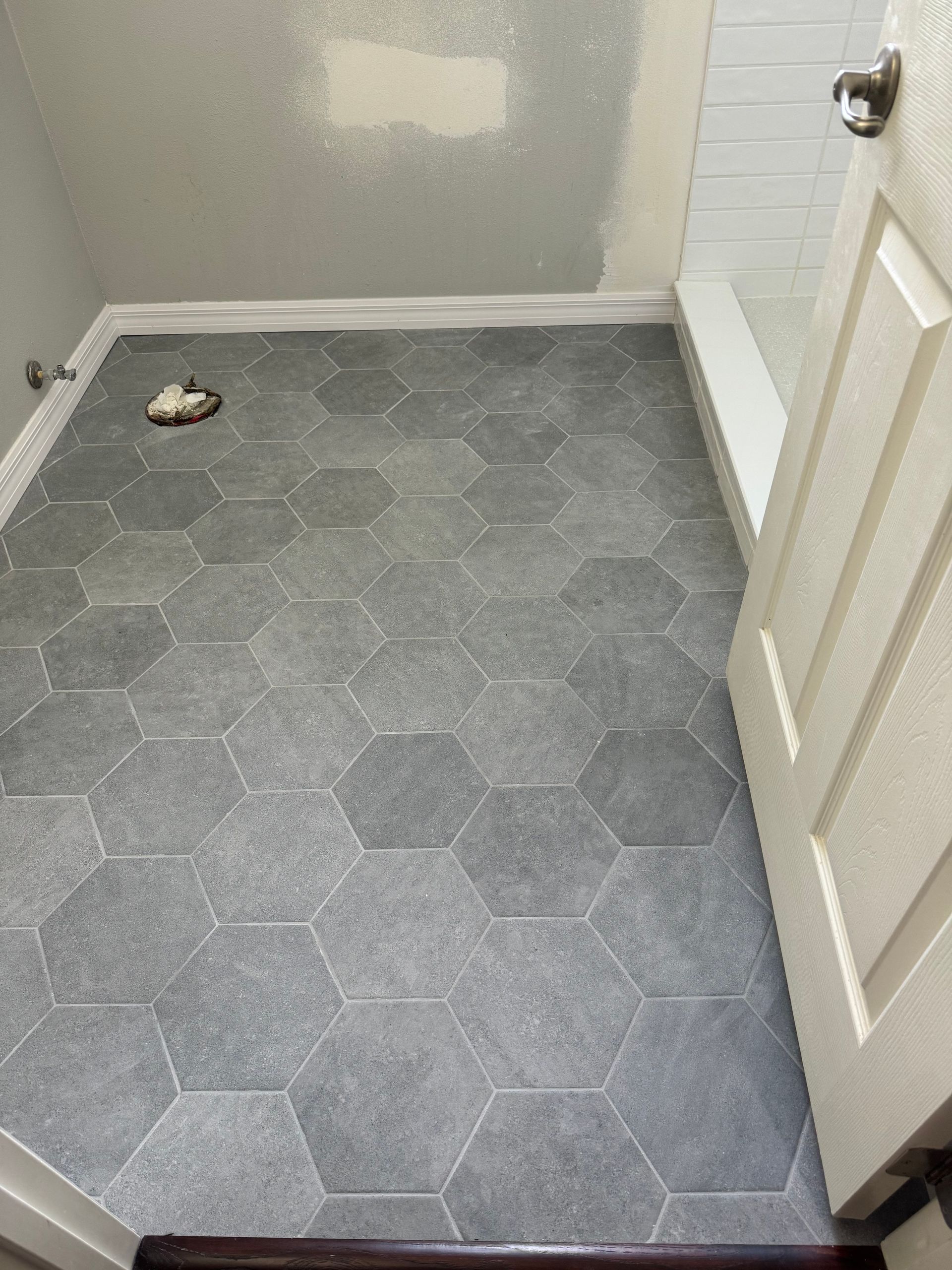 Small bathroom with gray hex tile floor, toilet paper on the floor, and a partially open door.
