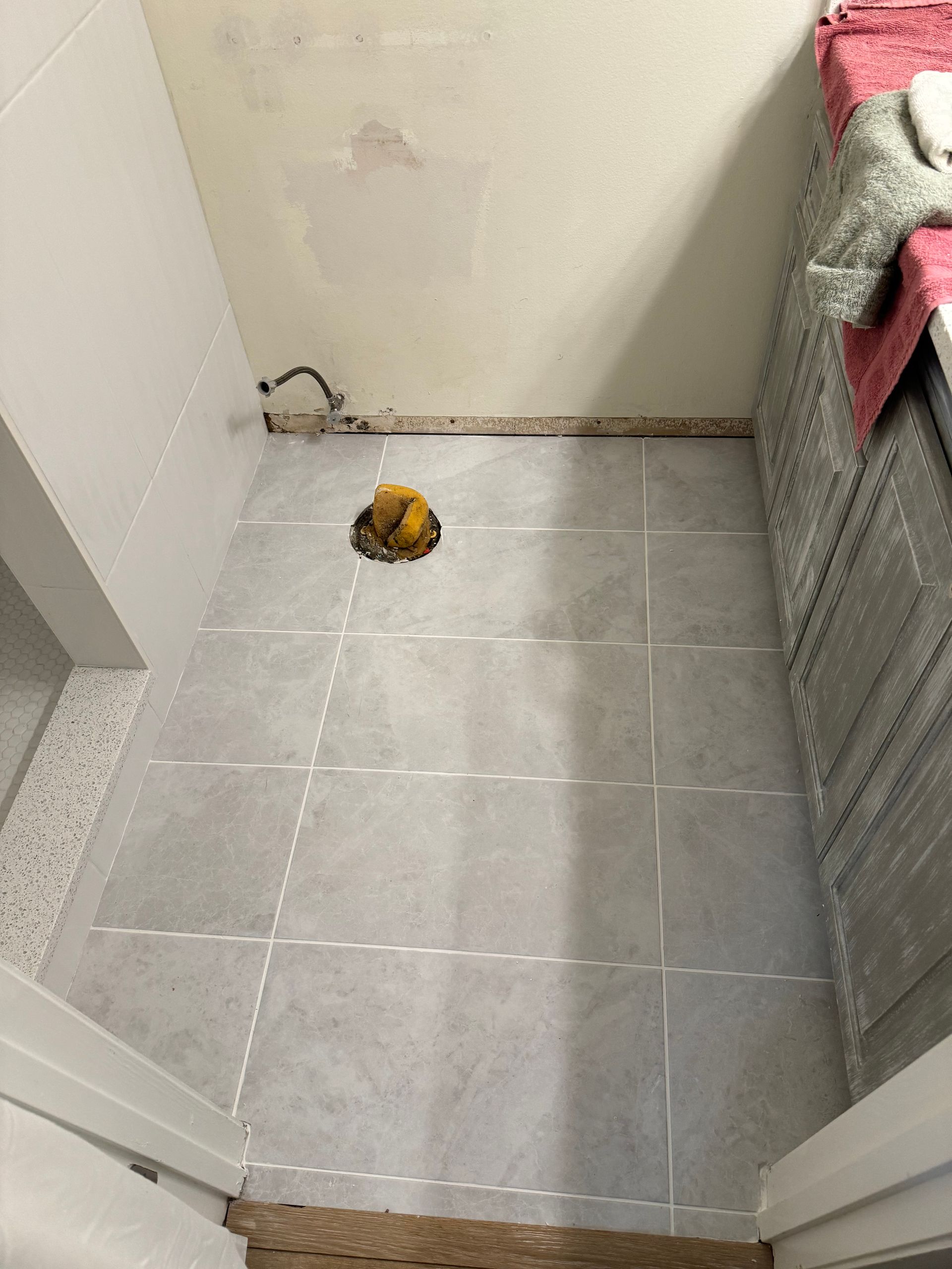 Small tiled bathroom with a yellow object near the back wall and a towel on the right.