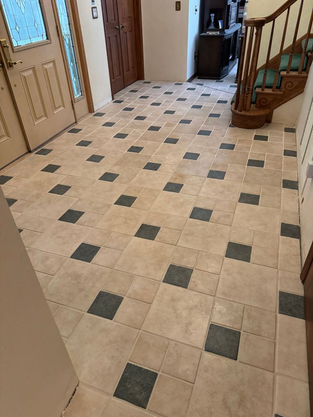 Interior hallway with beige tile floor, dark square accents, wooden doors, and a staircase on the right