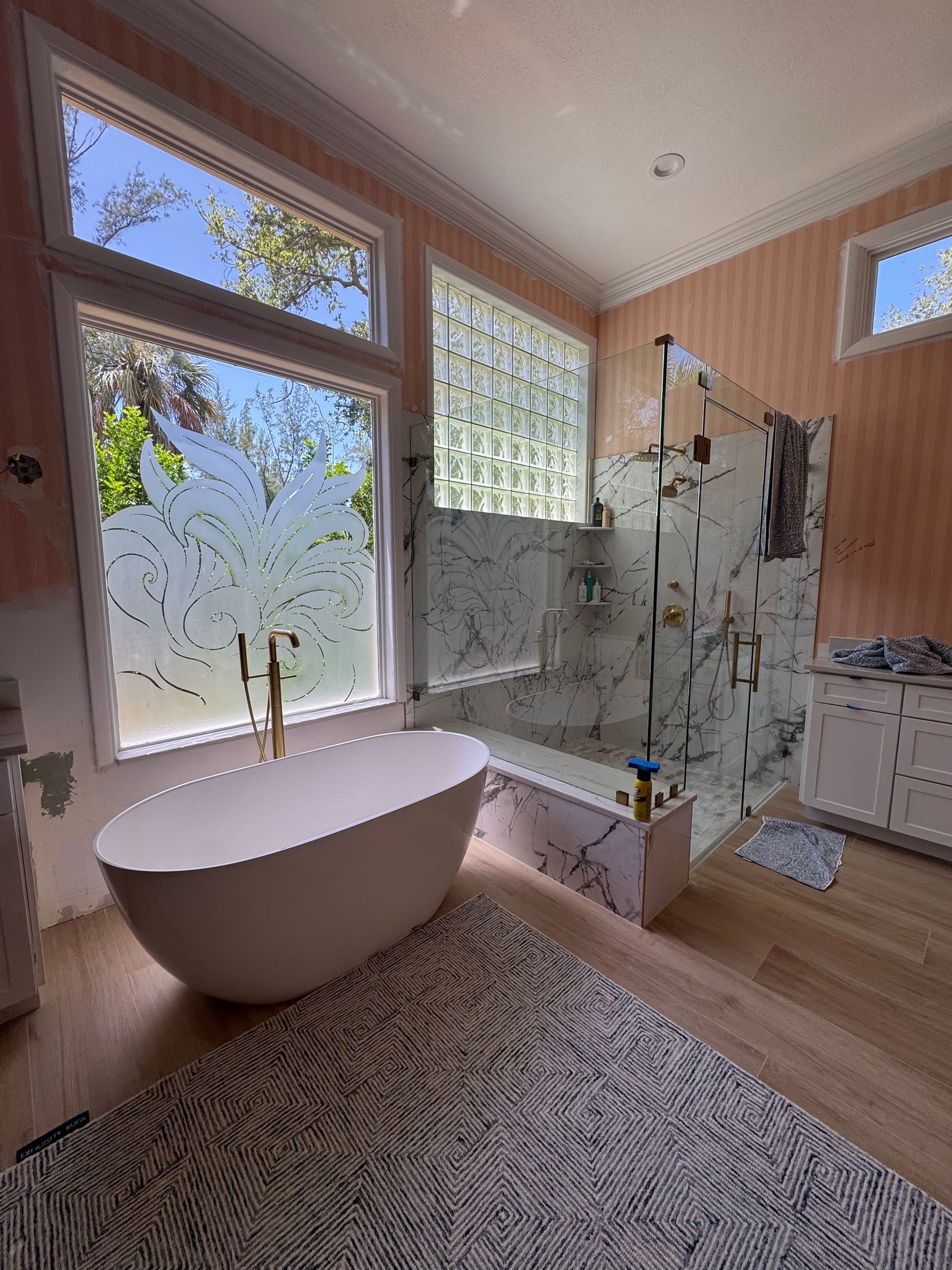 Modern bathroom with freestanding tub, glass shower, wood accents, and a large window letting in daylight