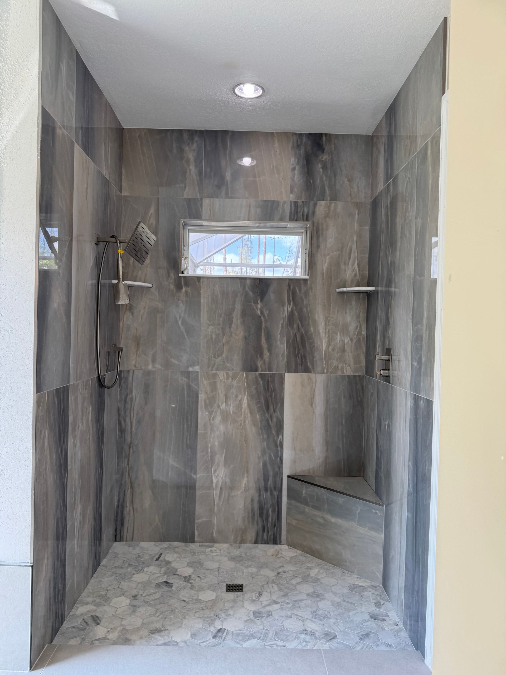 Modern tiled walk-in shower with a glass block window, handheld showerhead, and bench.