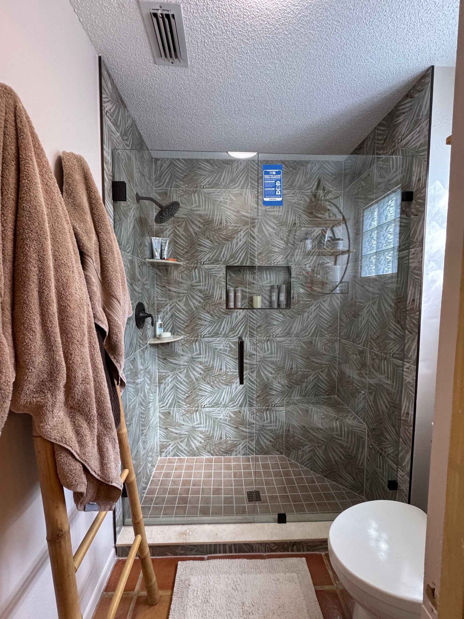 Modern tiled shower with glass door, built-in shelves, window, and a white toilet in the foreground