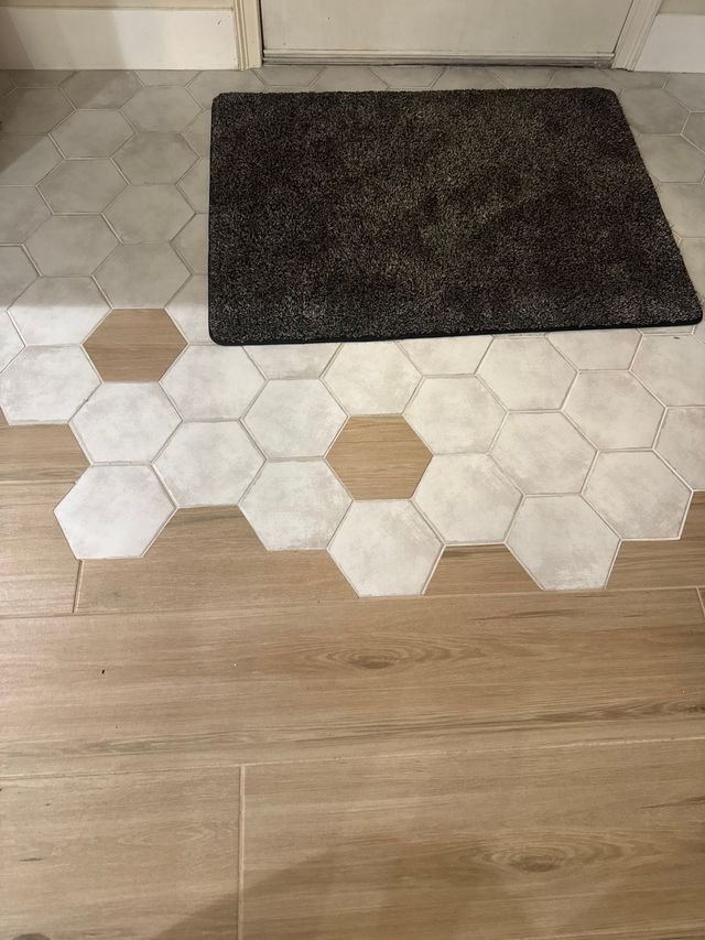 Entryway with a dark doormat on white and tan hex tile flooring beside wood laminate floor.