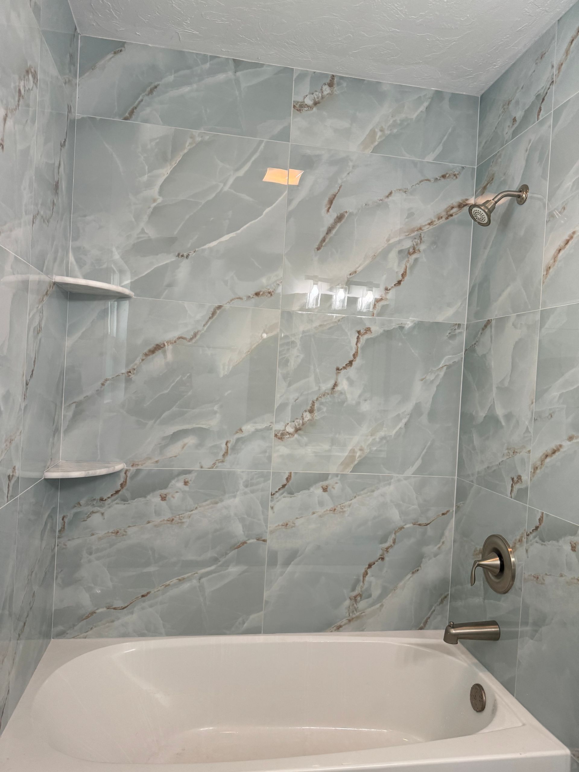 Small bathroom with gray marble tile walls, a white bathtub, and chrome shower fixtures.