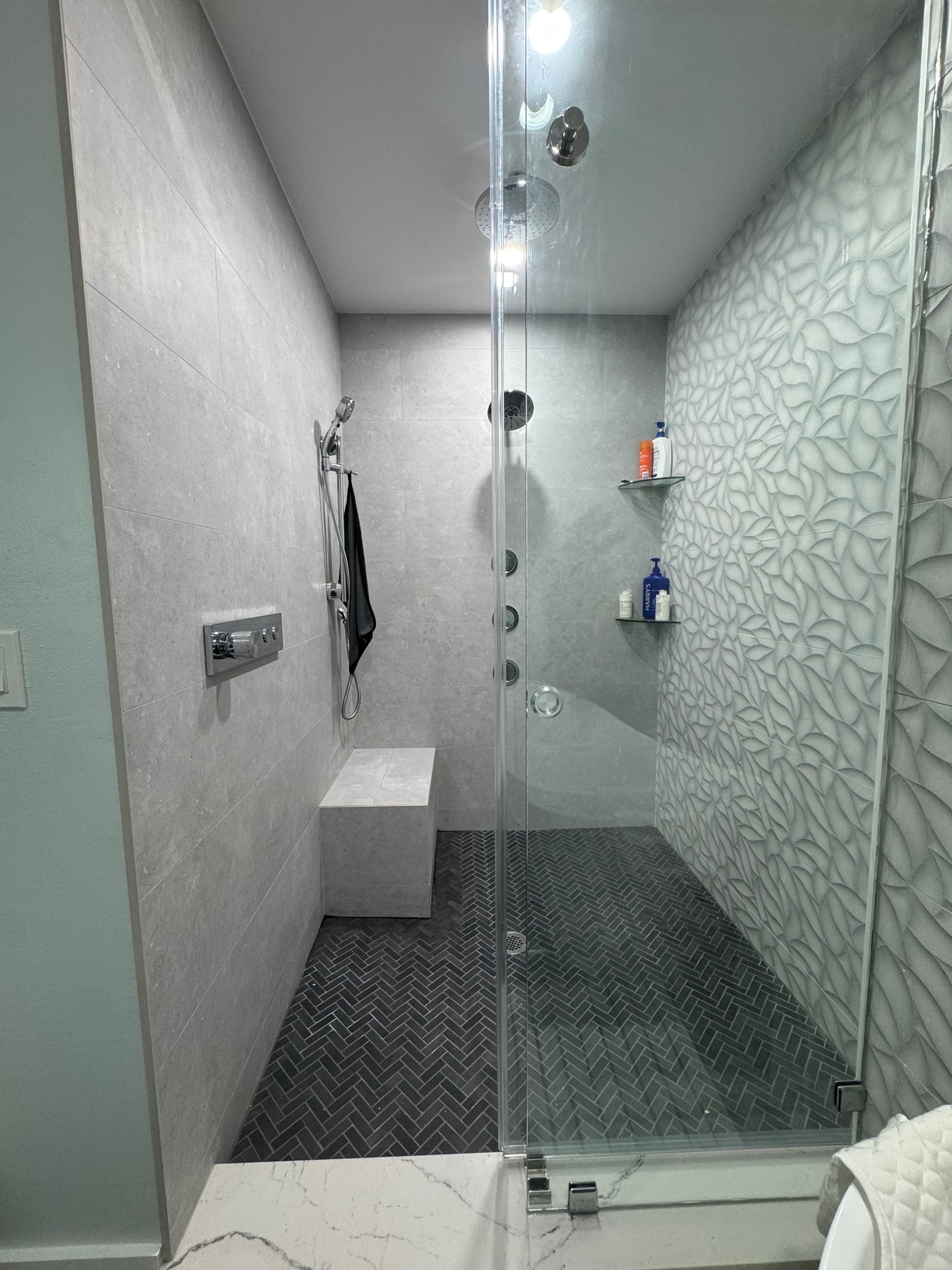 Modern tiled shower with glass door, white bench, and chrome fixtures