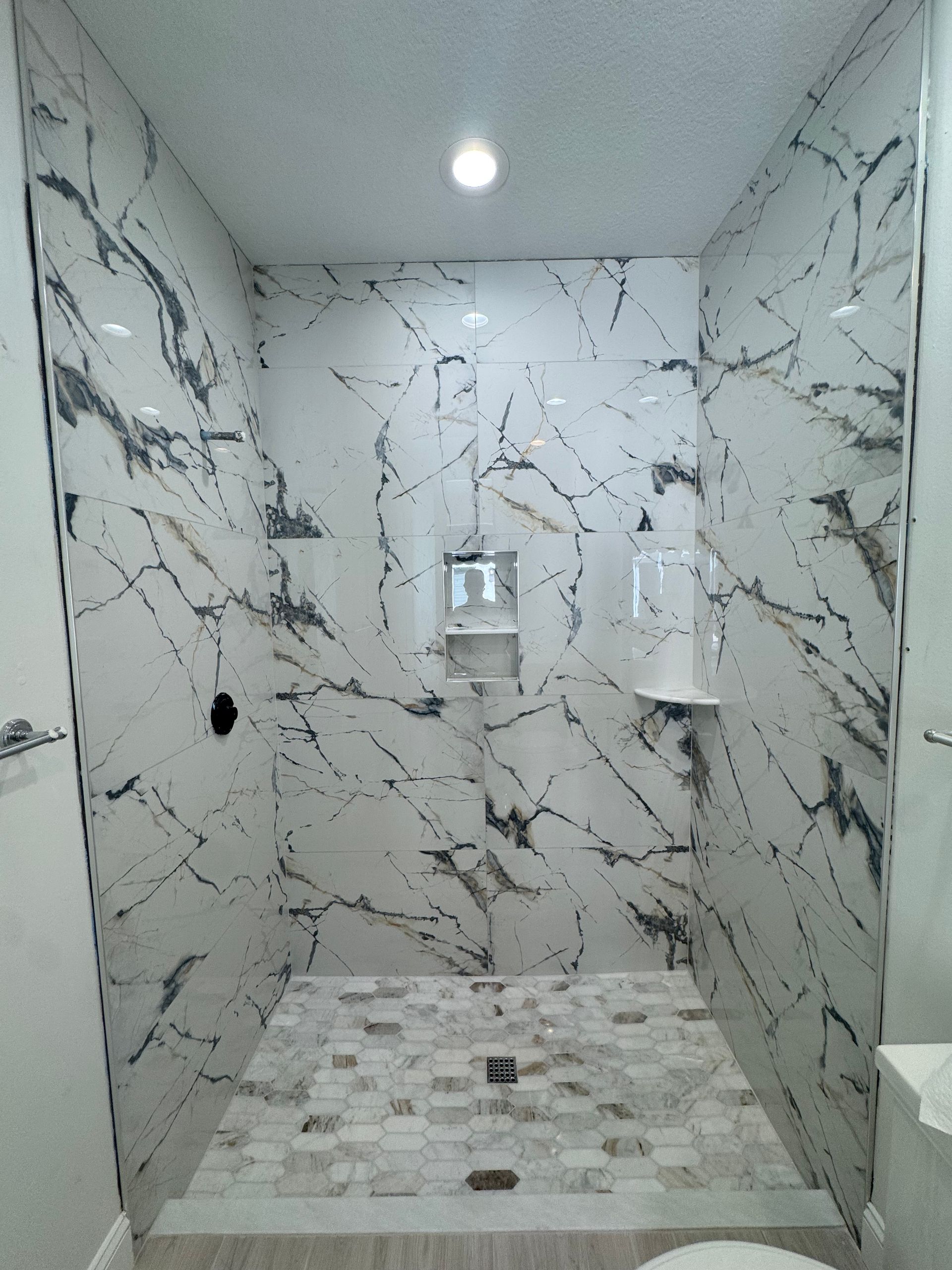 Marble-tiled shower stall with built-in shelves, a bench, and a tiled floor drain