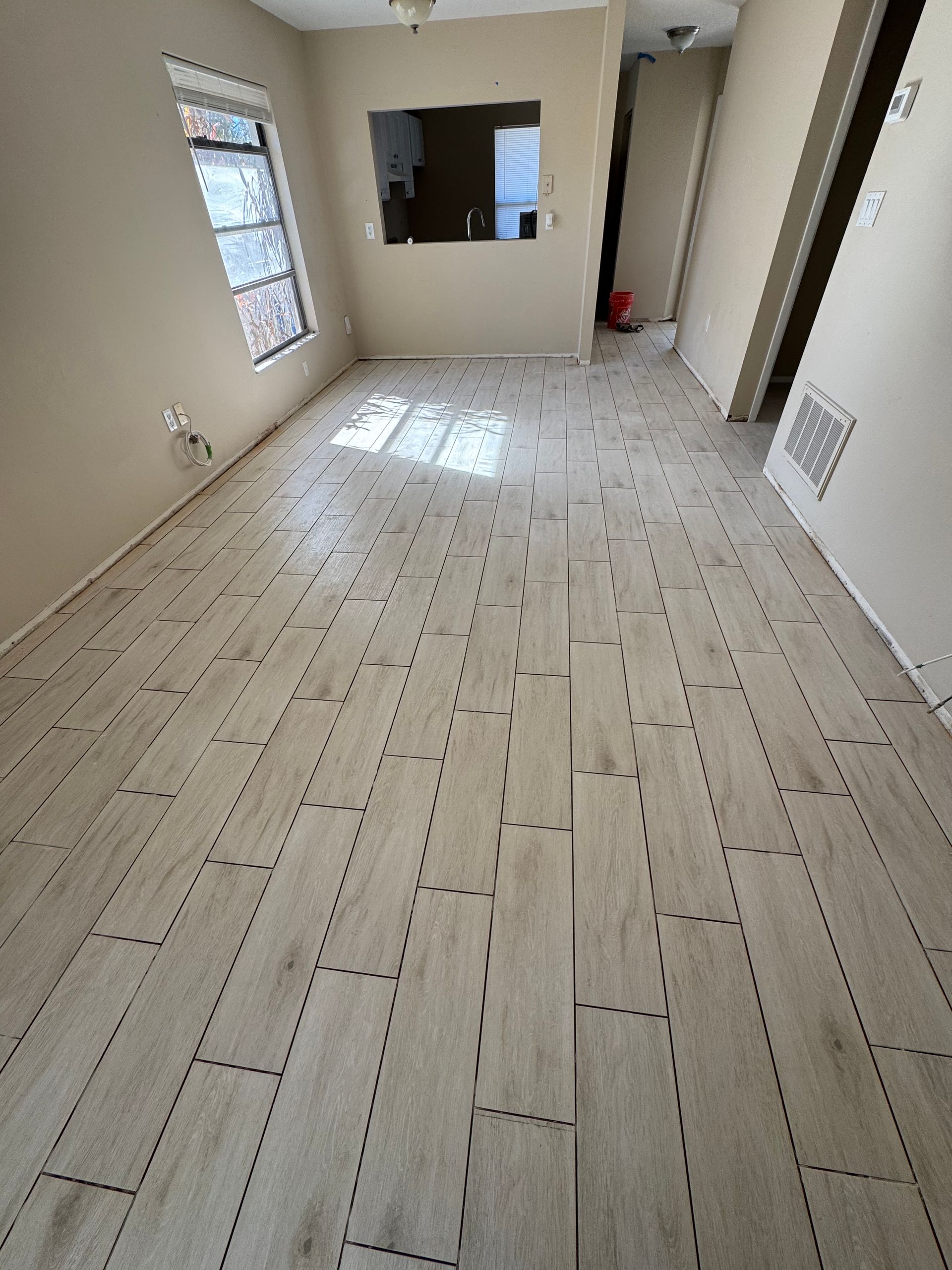 Empty beige-tiled room with window, pass-through opening, and doorway.