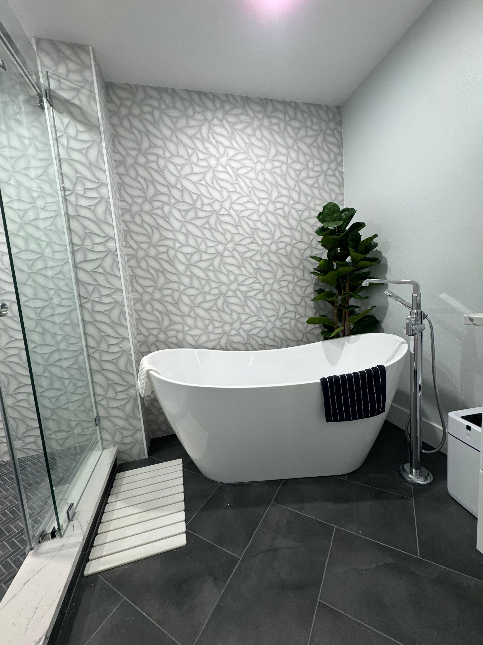 Modern bathroom with freestanding tub, glass shower, patterned walls, and dark tile floor