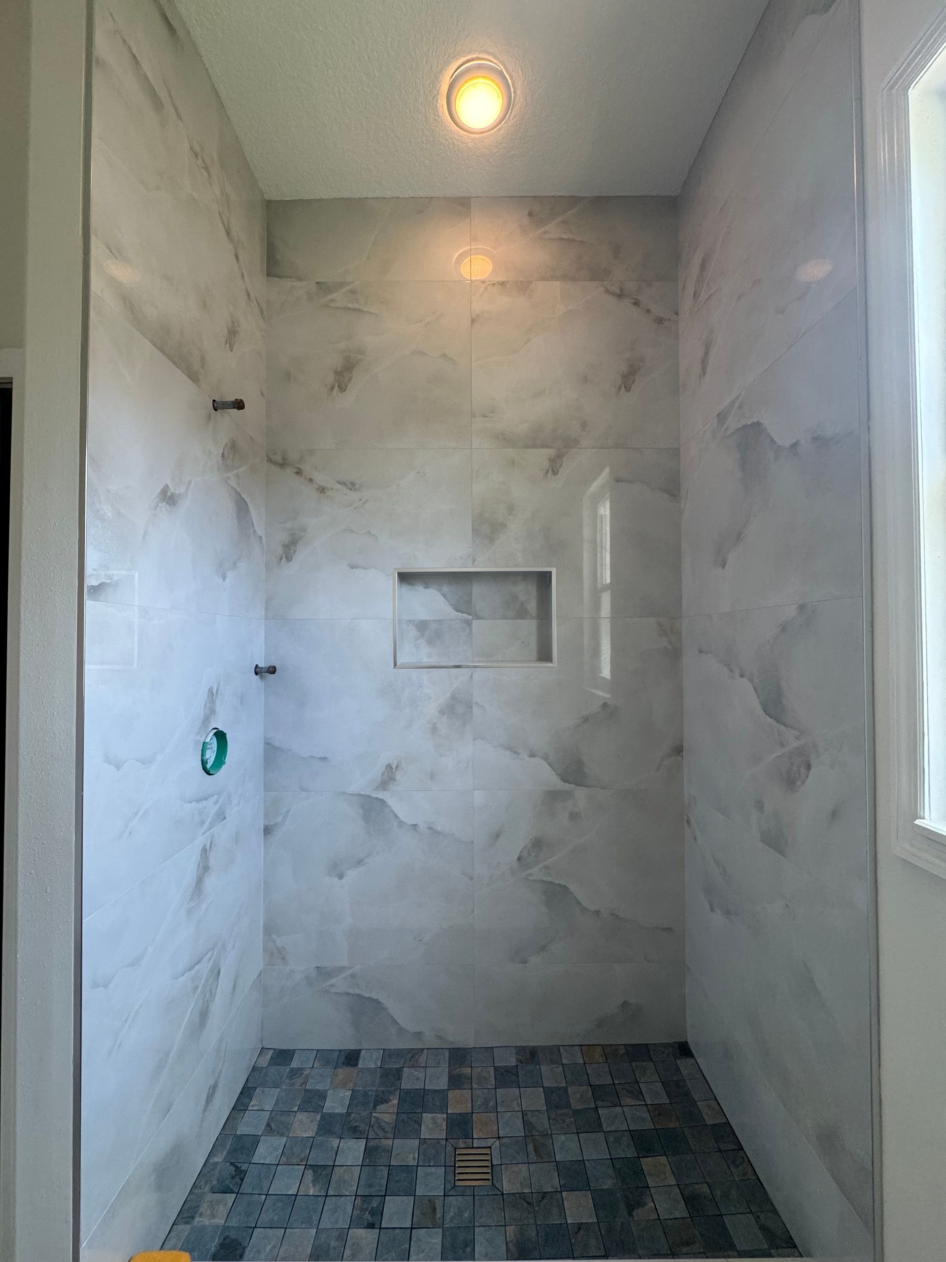 Empty tiled shower stall with marble-look walls and a recessed shelf under a ceiling light