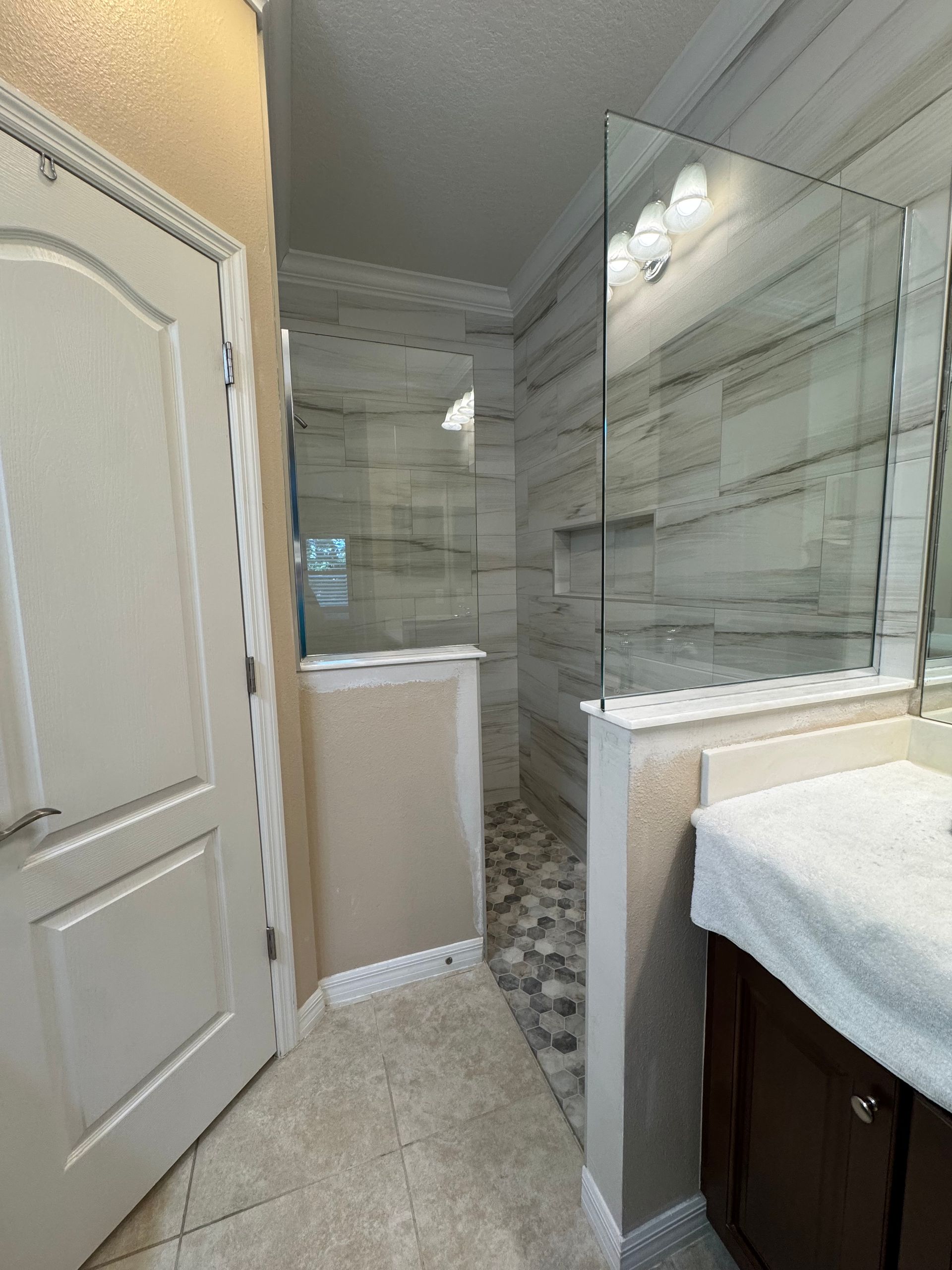 Narrow bathroom with a shower, glass partition, beige tile floor, and vanity sink