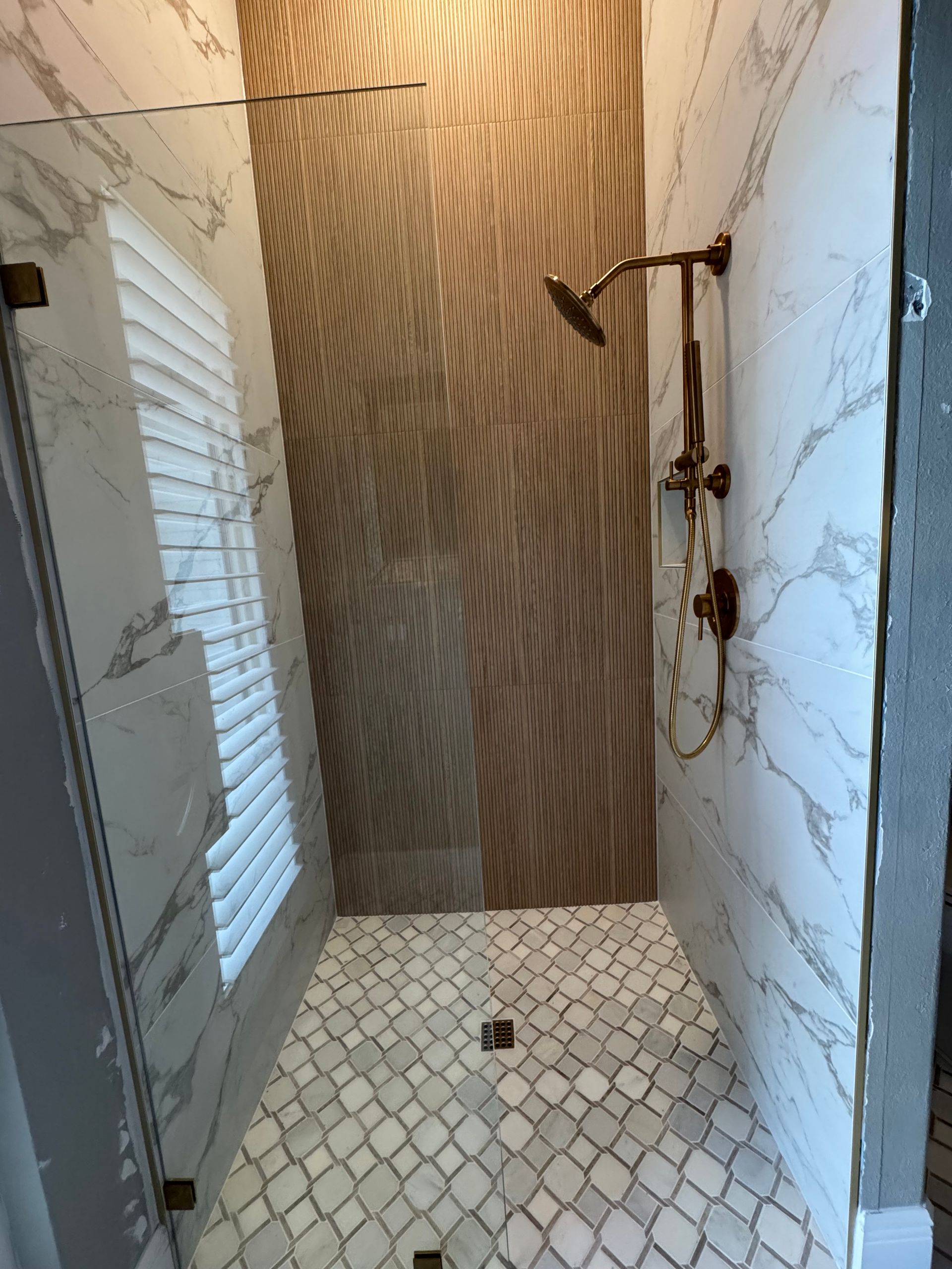 Small tiled bathroom shower stall with white walls, wood-look back wall, and a window on the left.