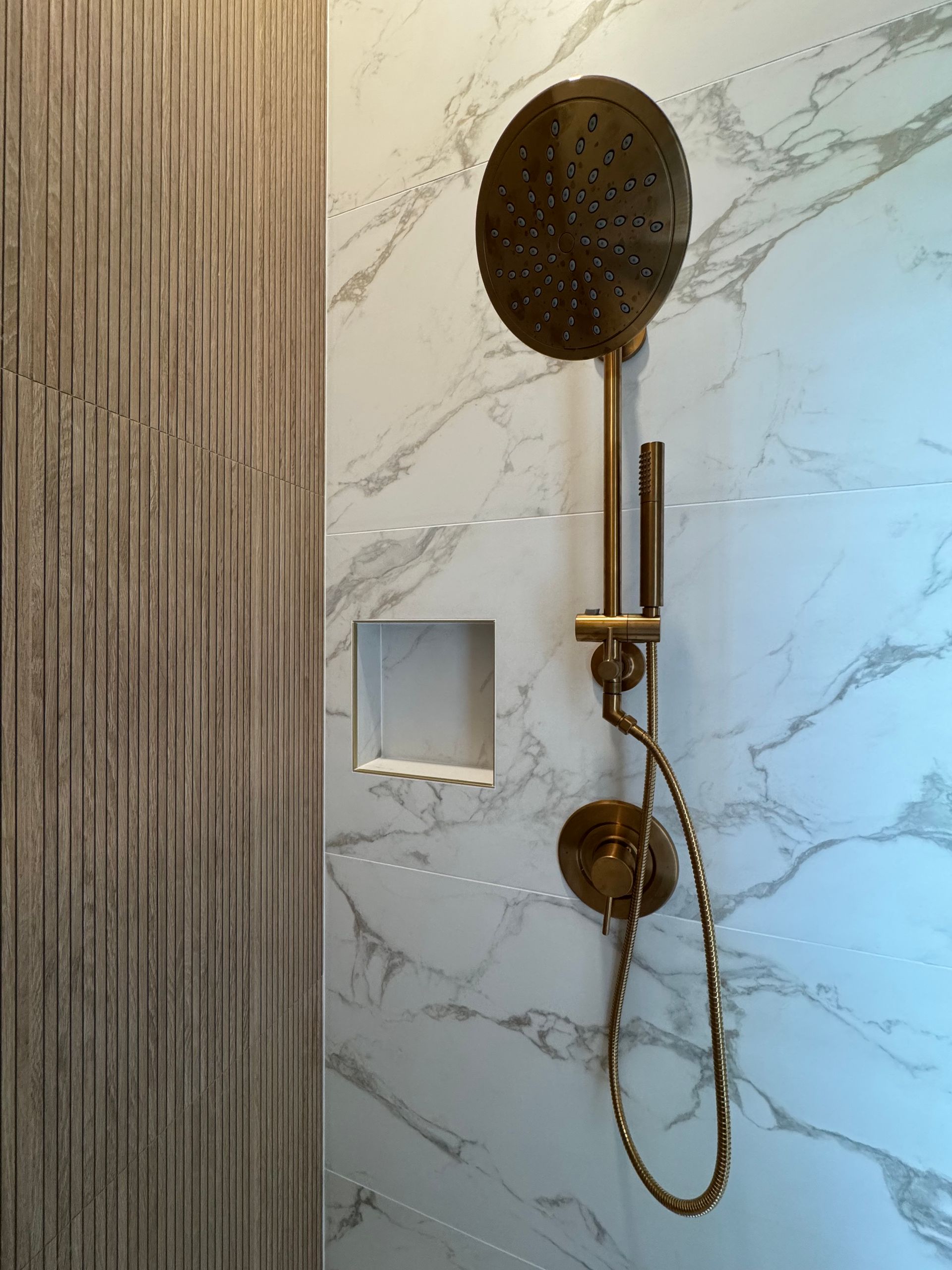 Modern shower with marble-look tile, black showerhead, brass fixtures, and a handheld sprayer