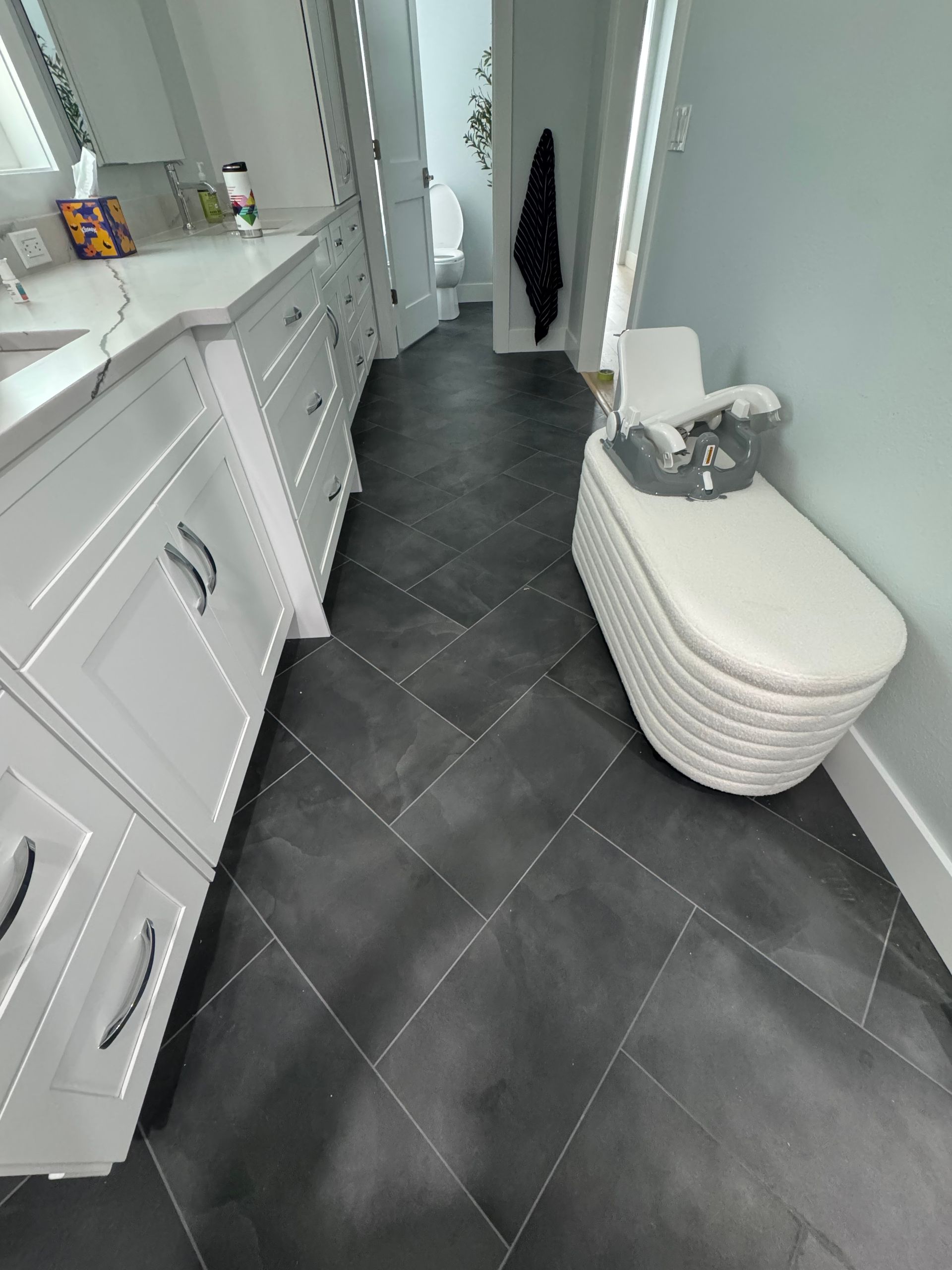 Narrow bathroom with white cabinets, dark tiled floor, and a white toilet or storage bench along the wall