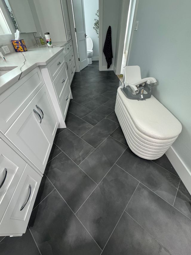 Narrow bathroom with white cabinets, gray tile floor, and a woven hamper along the wall