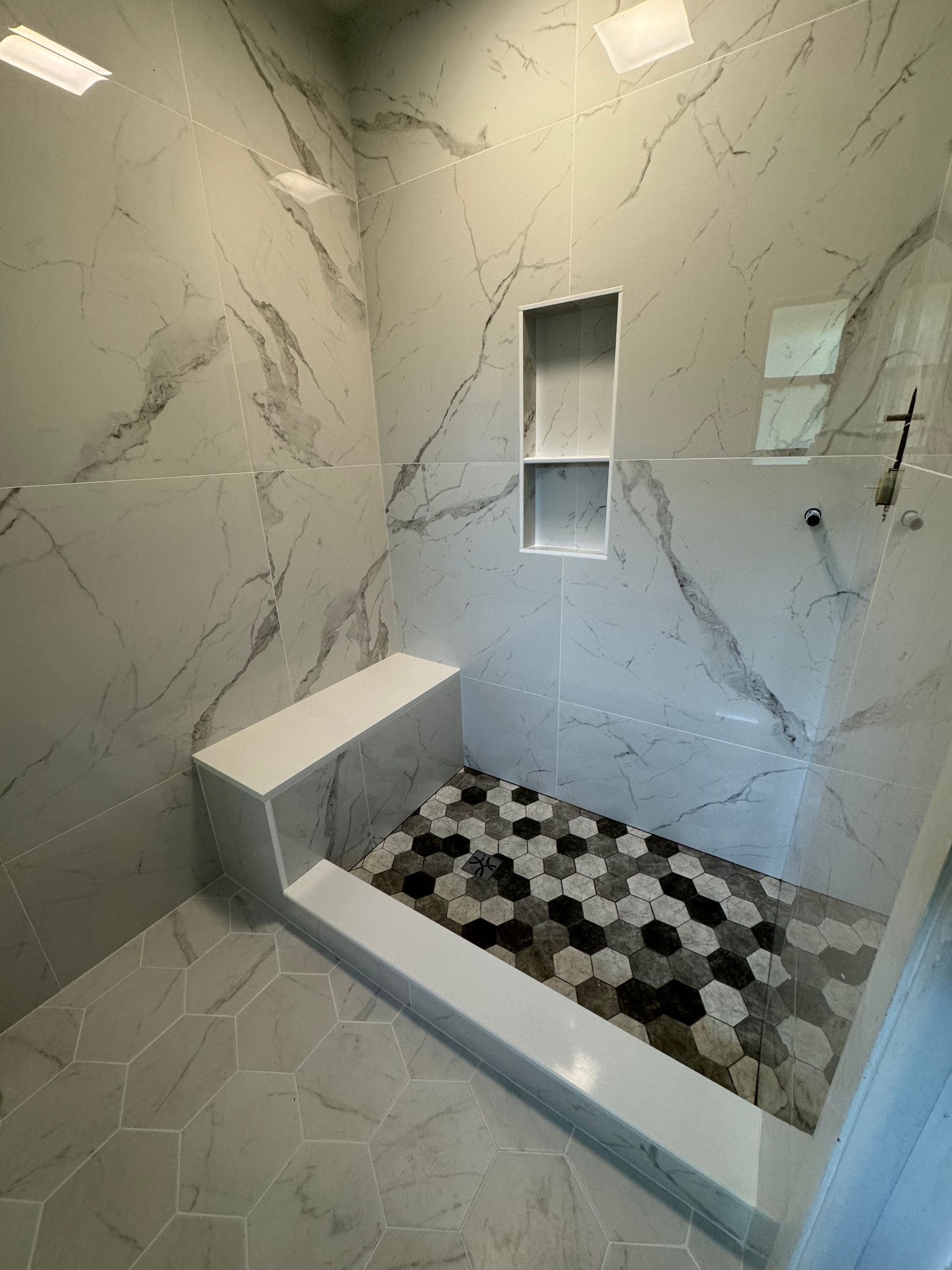 Modern tiled shower with marble-look walls, built-in bench, and black-and-white pebble floor