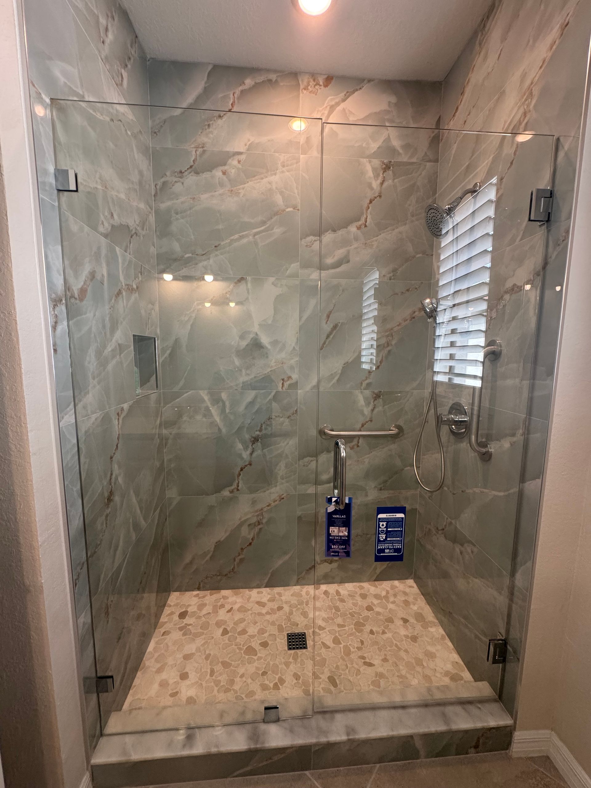 Glass walk-in shower with marble tile, bench, and shower fixtures in a modern bathroom.