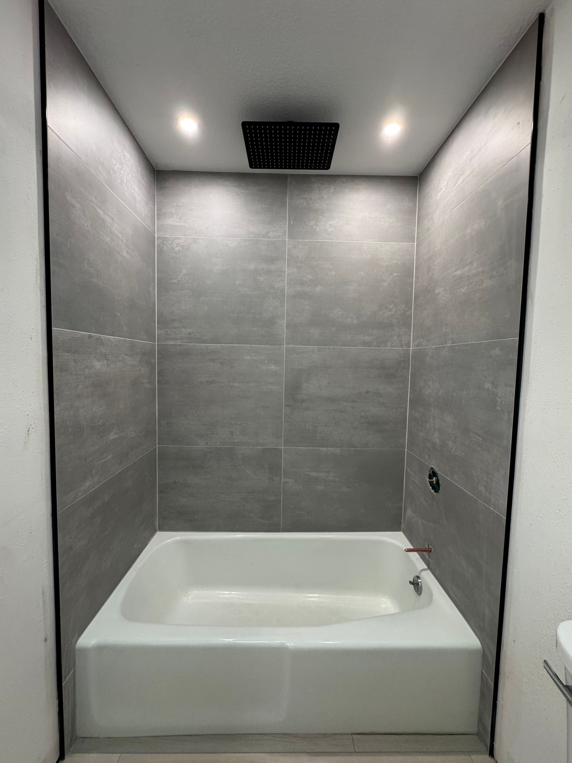 Modern gray-tiled bathroom with a white built-in bathtub and recessed ceiling lights