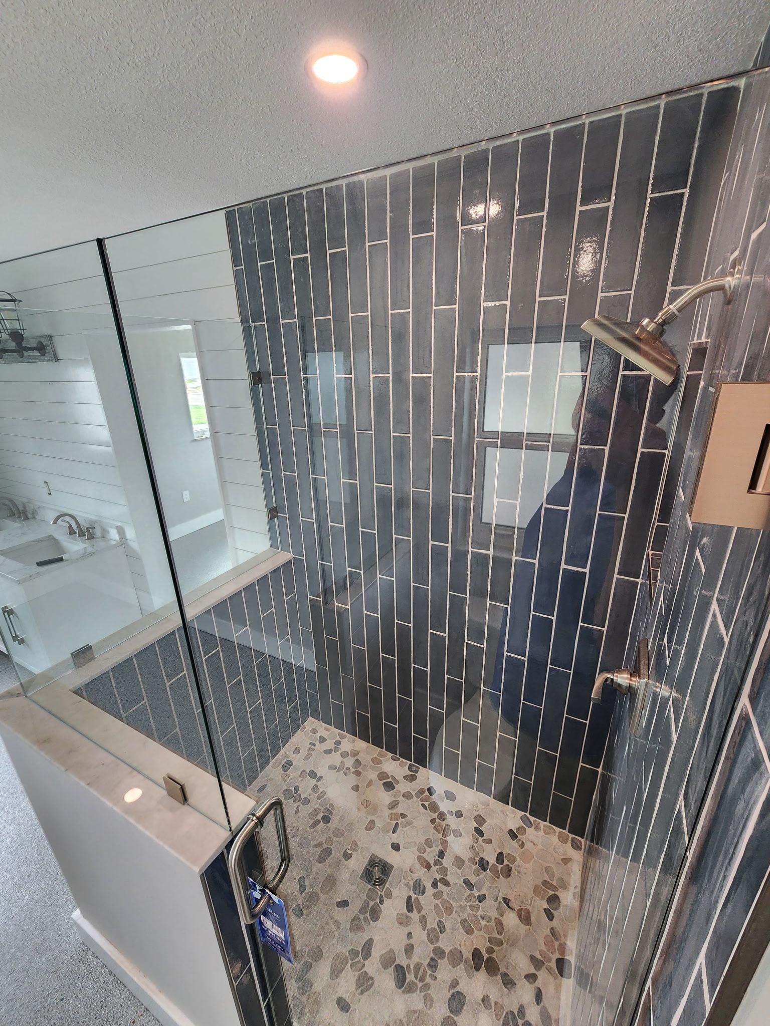 Modern shower with glass enclosure, black tile wall, and pebble stone floor in a bathroom.