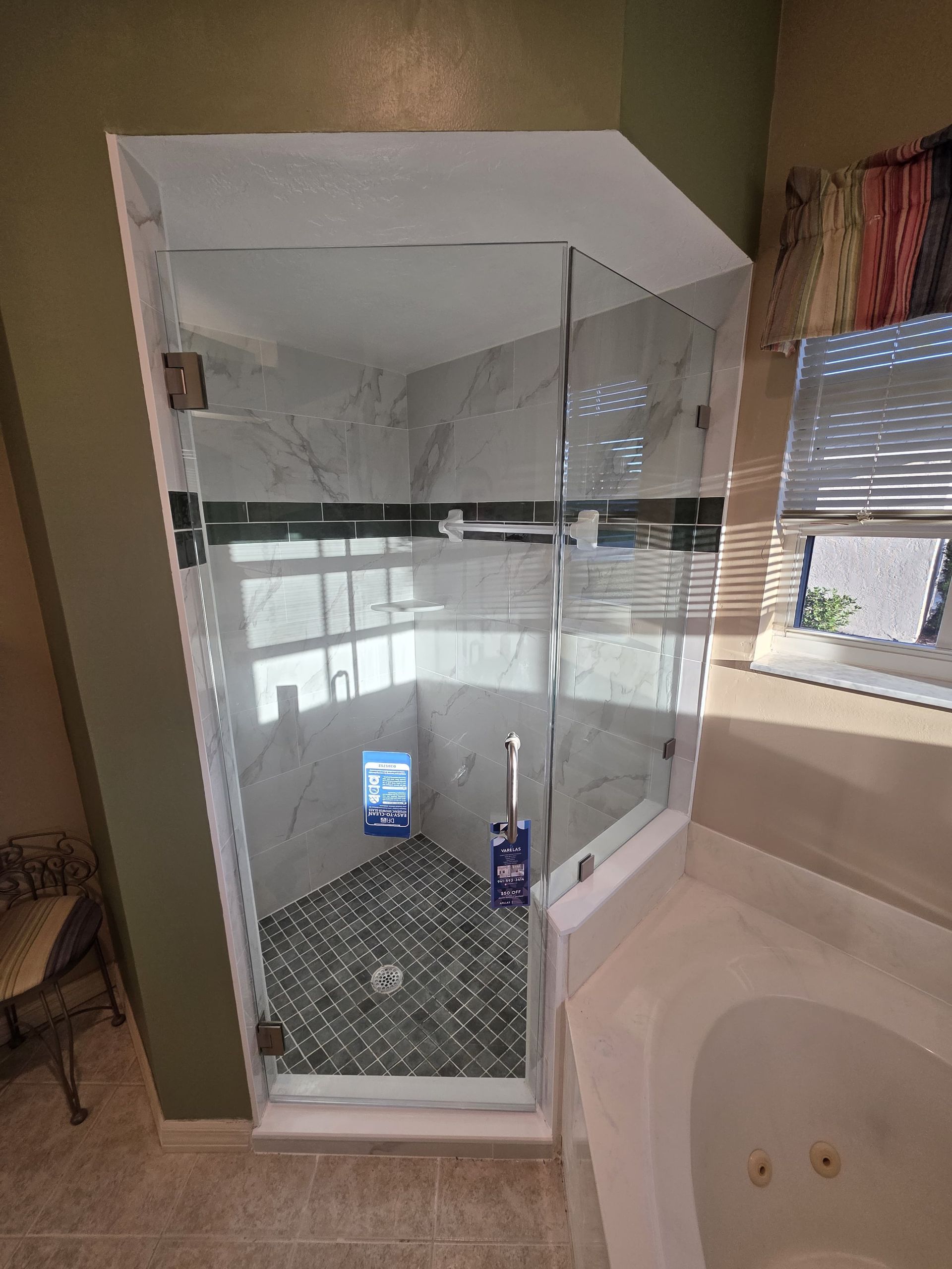 Glass shower stall beside a white bathtub in a bathroom, with a patterned tile floor and window light.