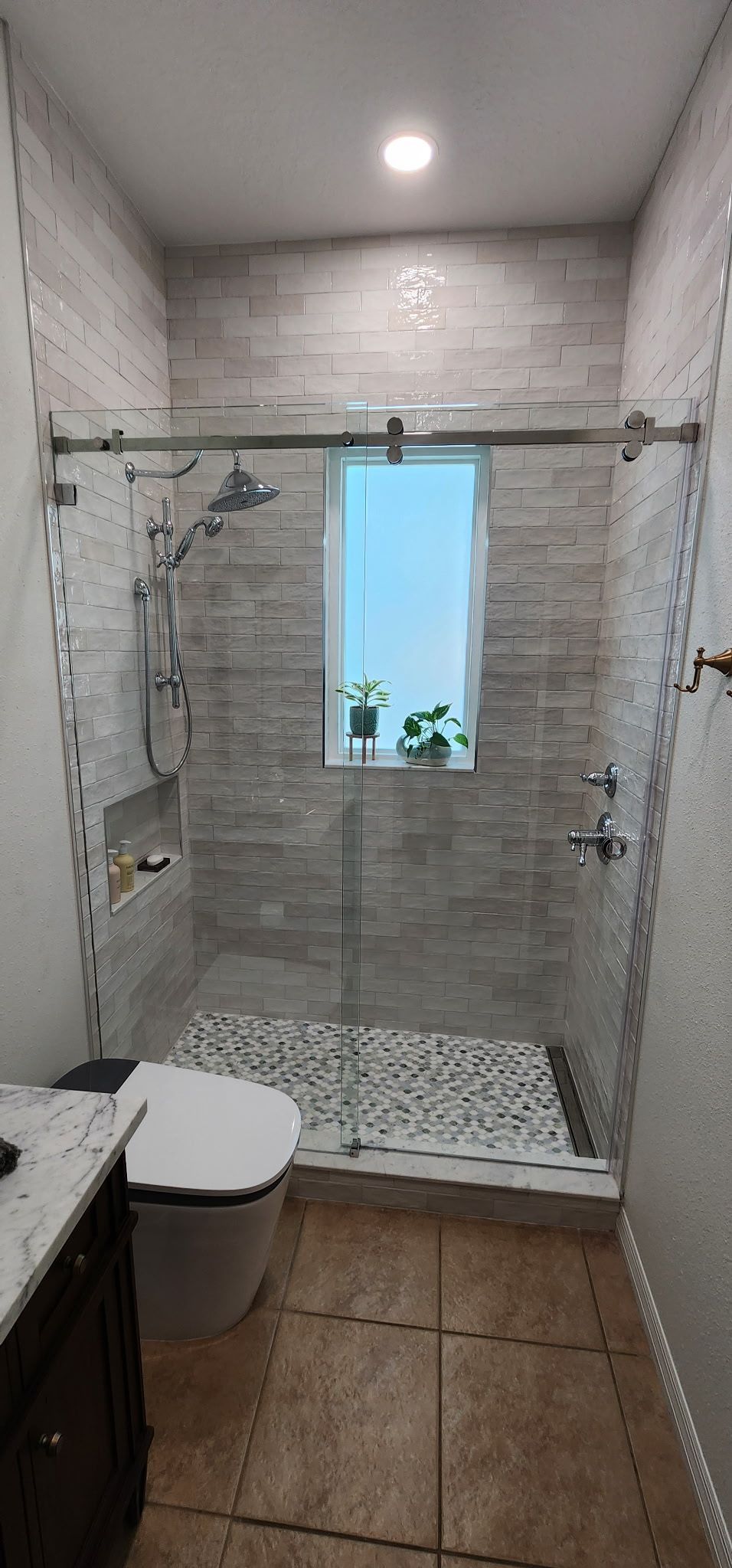 Small tiled bathroom with shower, toilet, and a narrow window