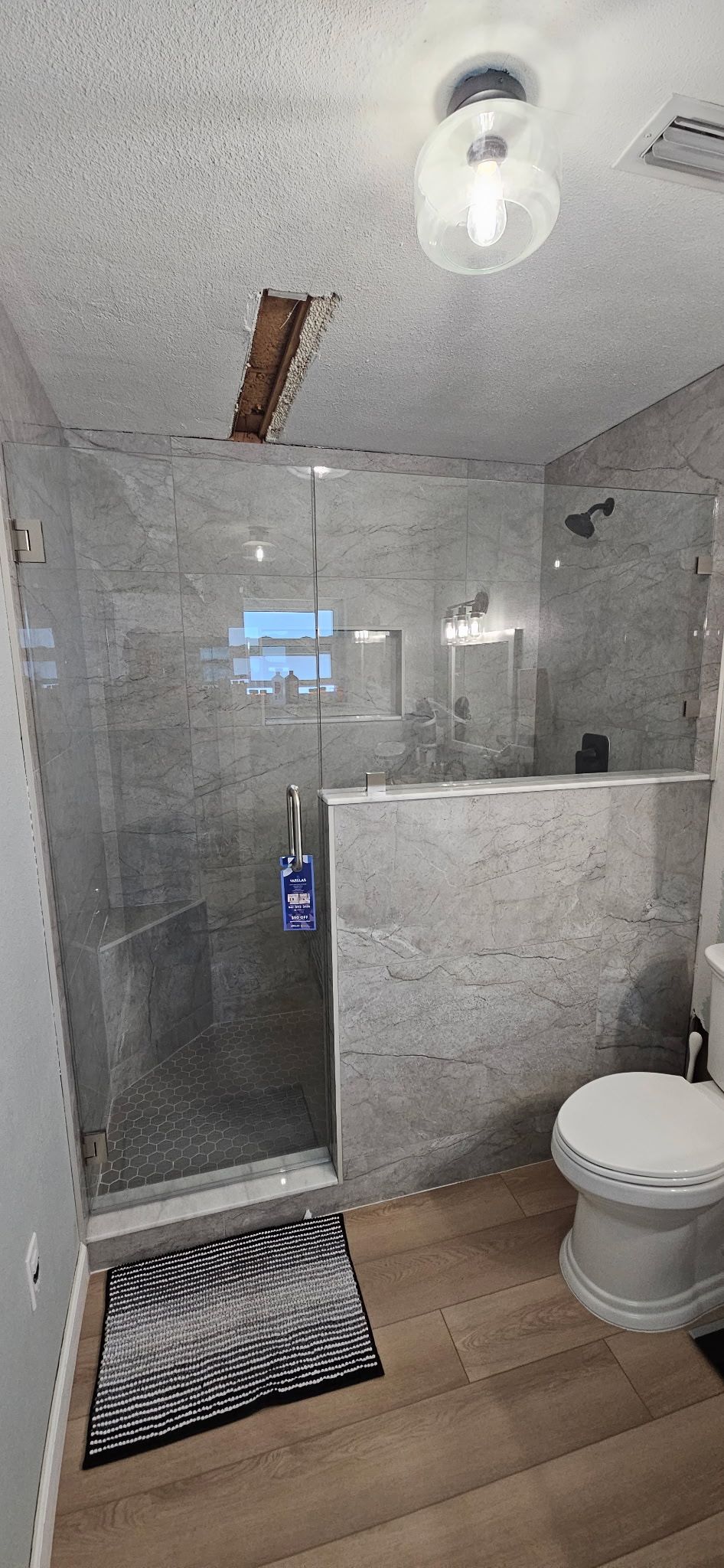 Small bathroom with glass shower, white toilet, wood floor, and exposed ceiling lights.
