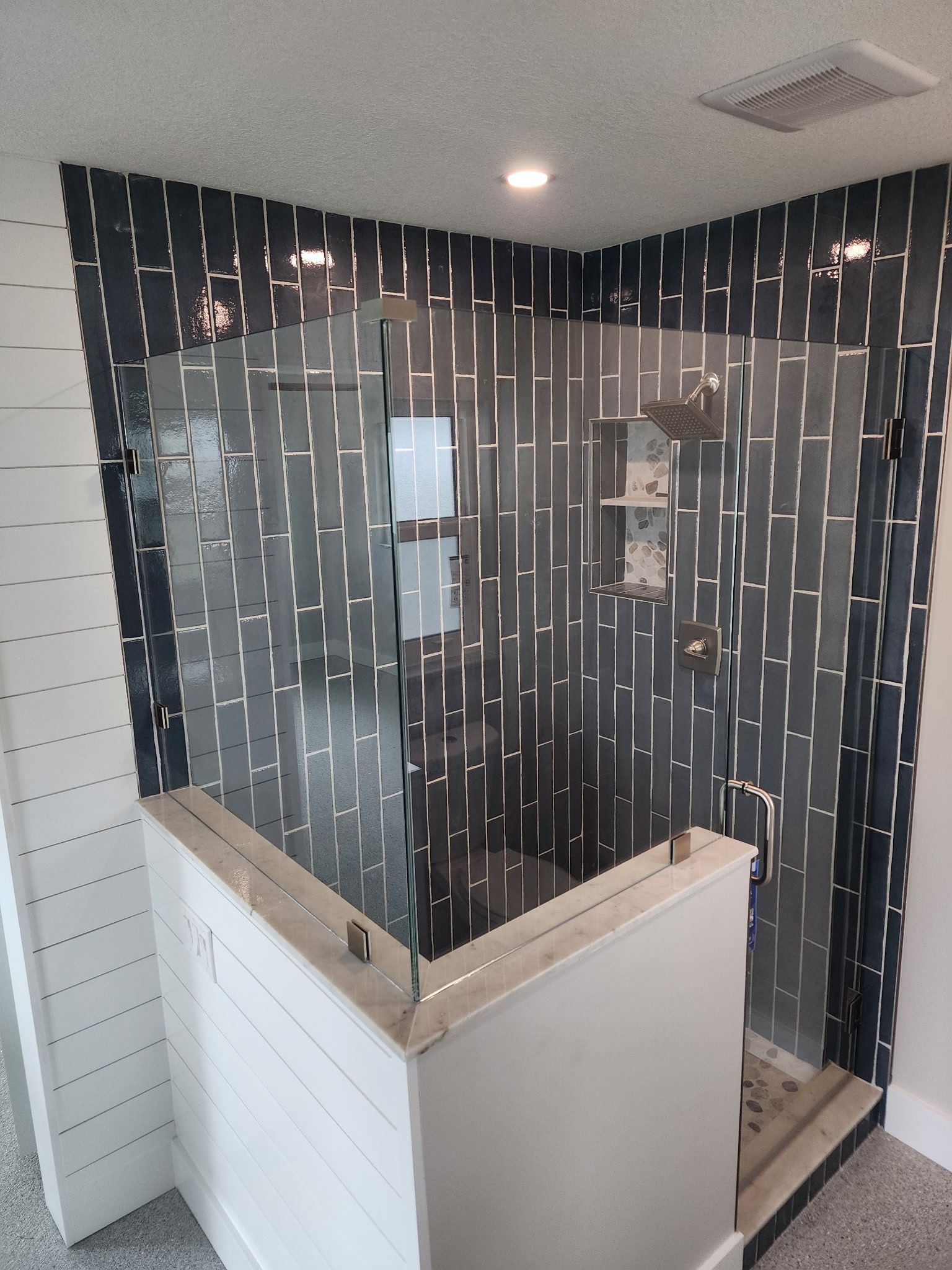 Small bathroom shower with black patterned glass walls and white tiled exterior.