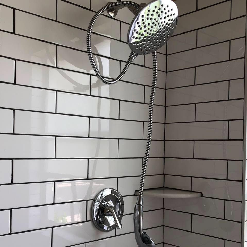 Chrome showerhead in a white-tiled shower stall with a hose and wall-mounted control.