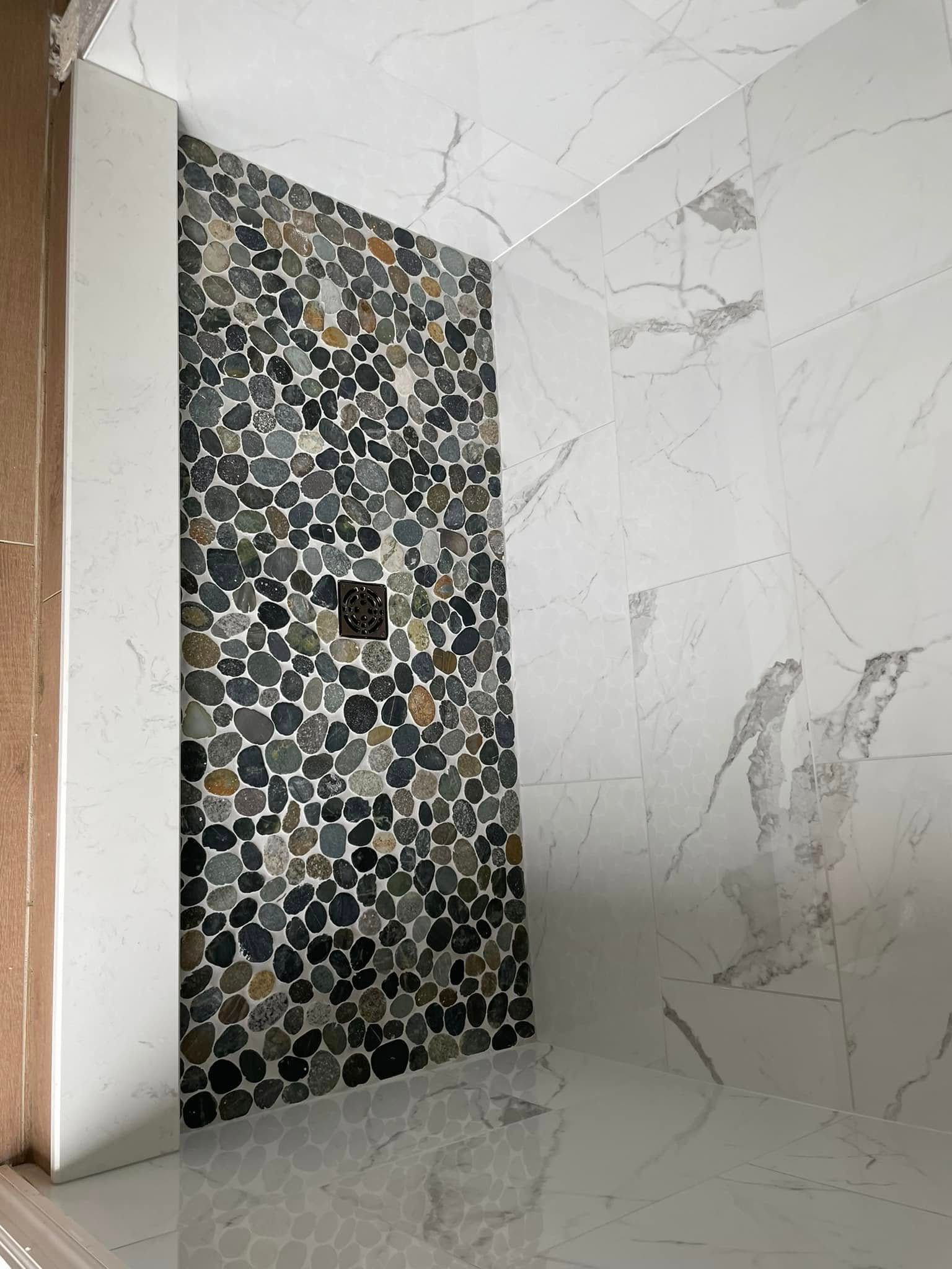 Modern bathroom with white marble-style tiles and a dark pebble mosaic accent wall