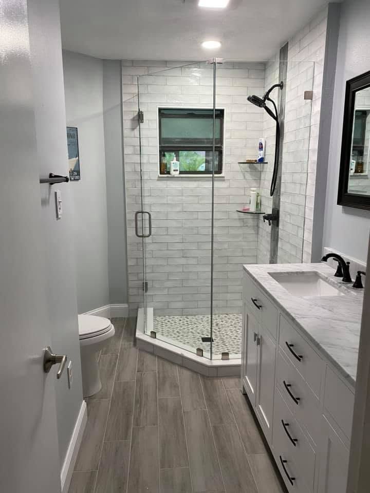 Modern bathroom with glass shower, white vanity, gray tile floor, and small window.