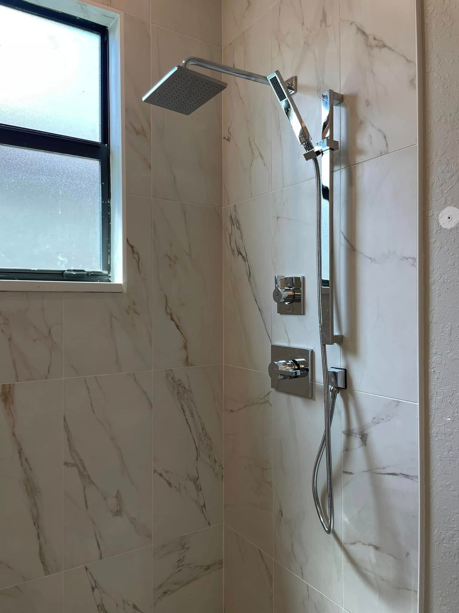 Modern bathroom shower with chrome fixtures, marble-look tile, and a frosted window