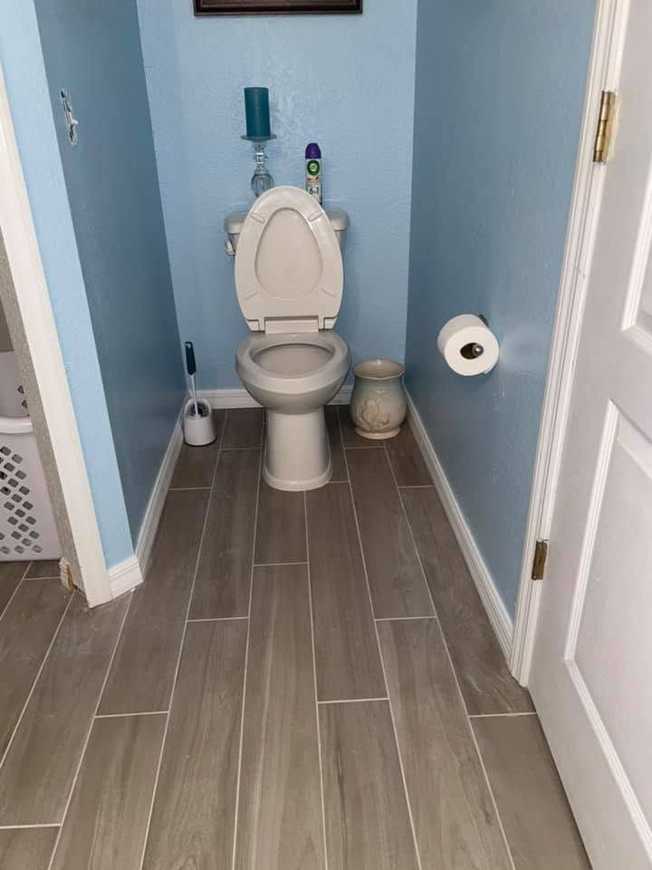 Small bathroom with a toilet, light blue walls, gray tile floor, and a toilet paper holder on the right.