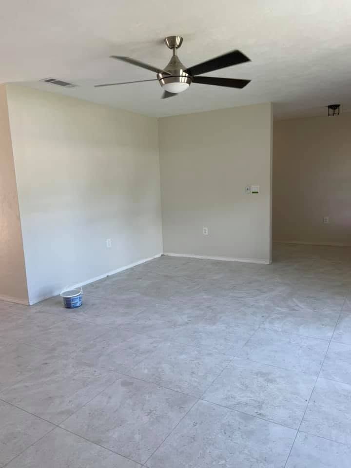 Empty tiled living room with white walls, ceiling fan, and a small paint can on the floor.