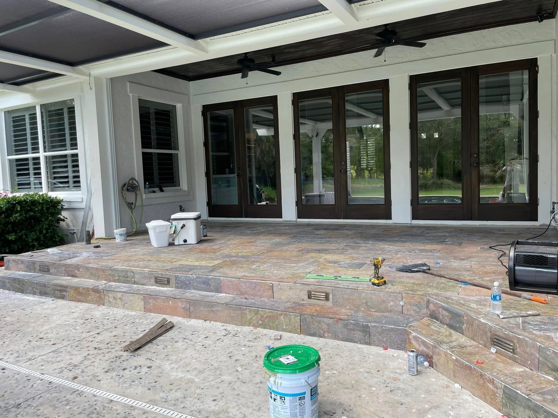 Patio with brick steps and glass doors under a covered porch, with buckets and tools scattered on the ground