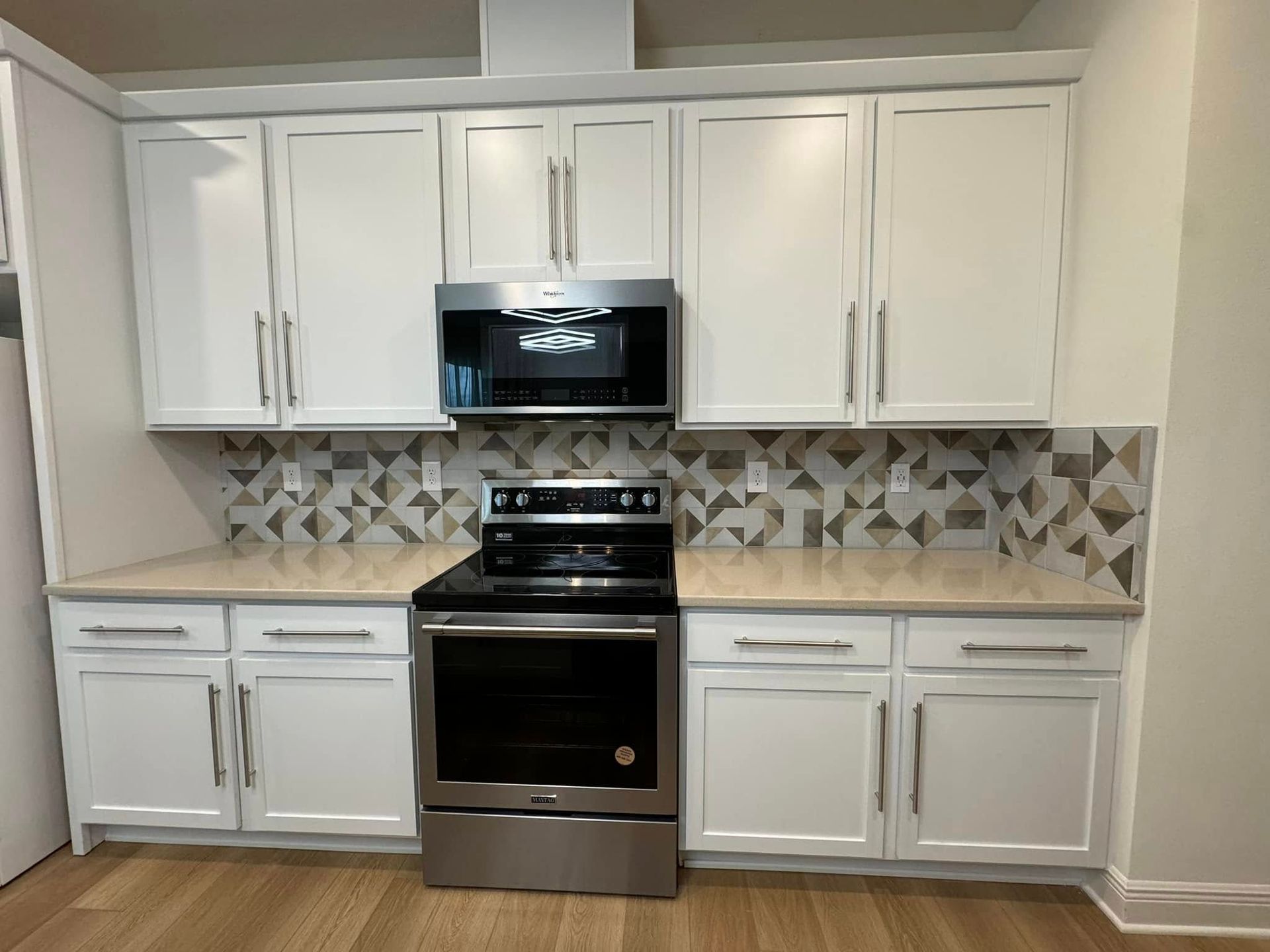 White kitchen with stainless steel stove and microwave, white cabinets, and geometric tile backsplash.