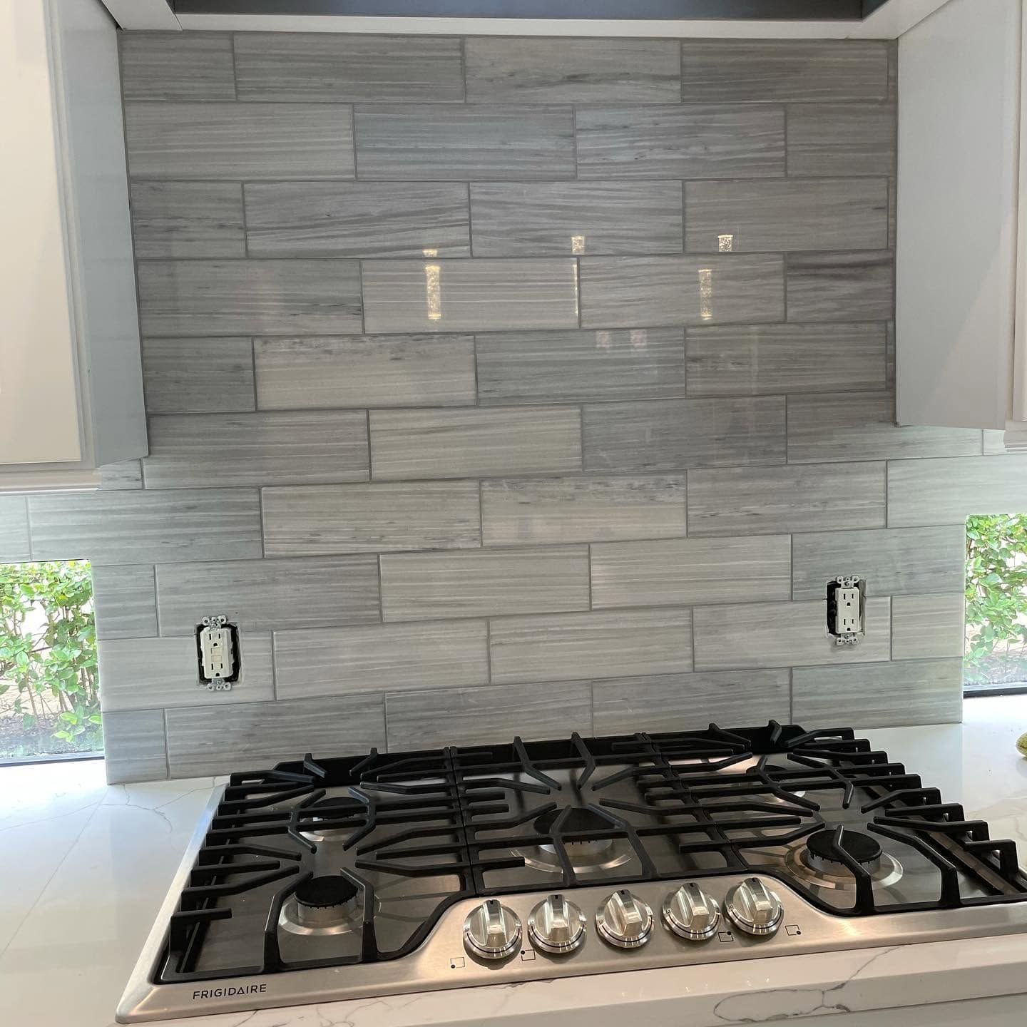 Modern kitchen stove with stainless steel range and gray tile backsplash under a vent hood