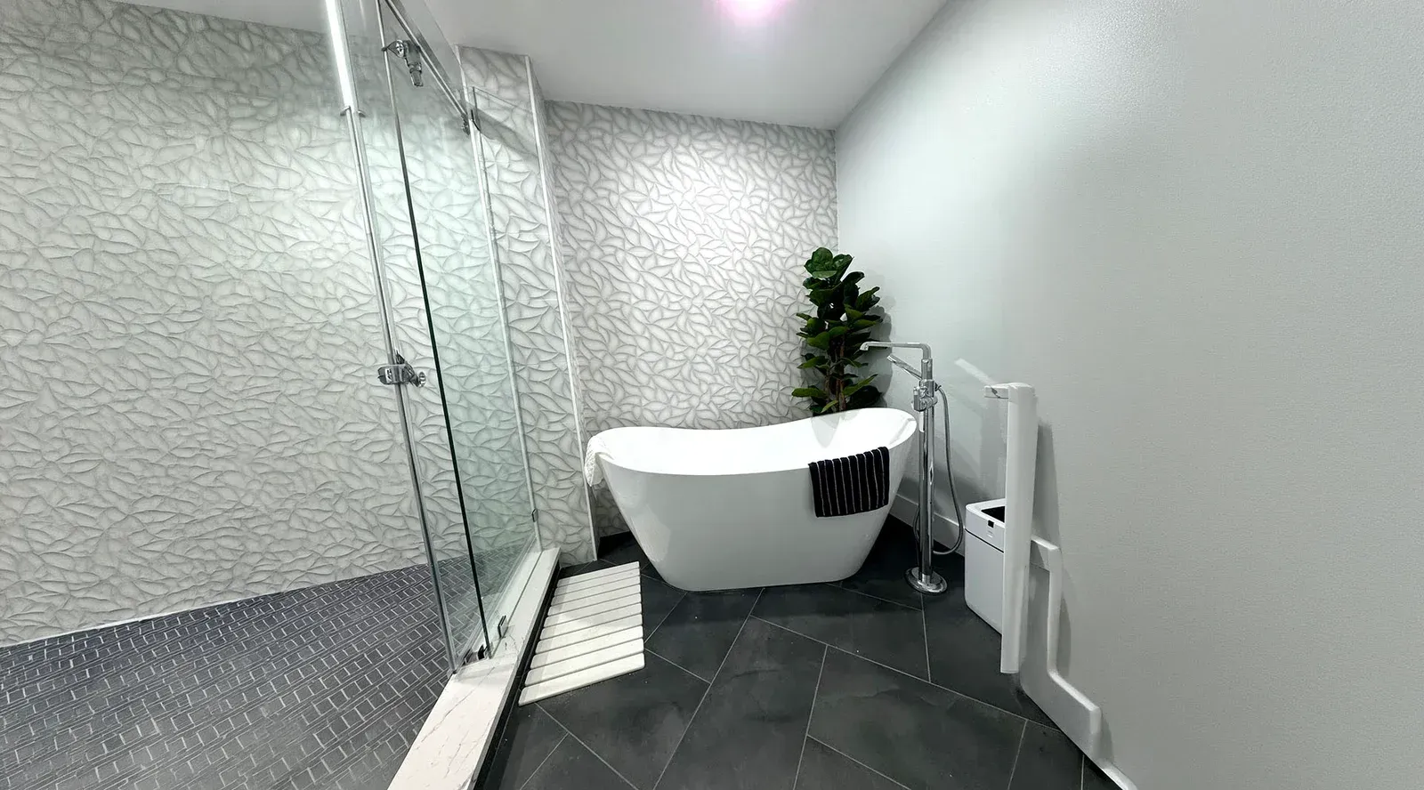 Modern bathroom with glass shower, freestanding white tub, and black tile floor.