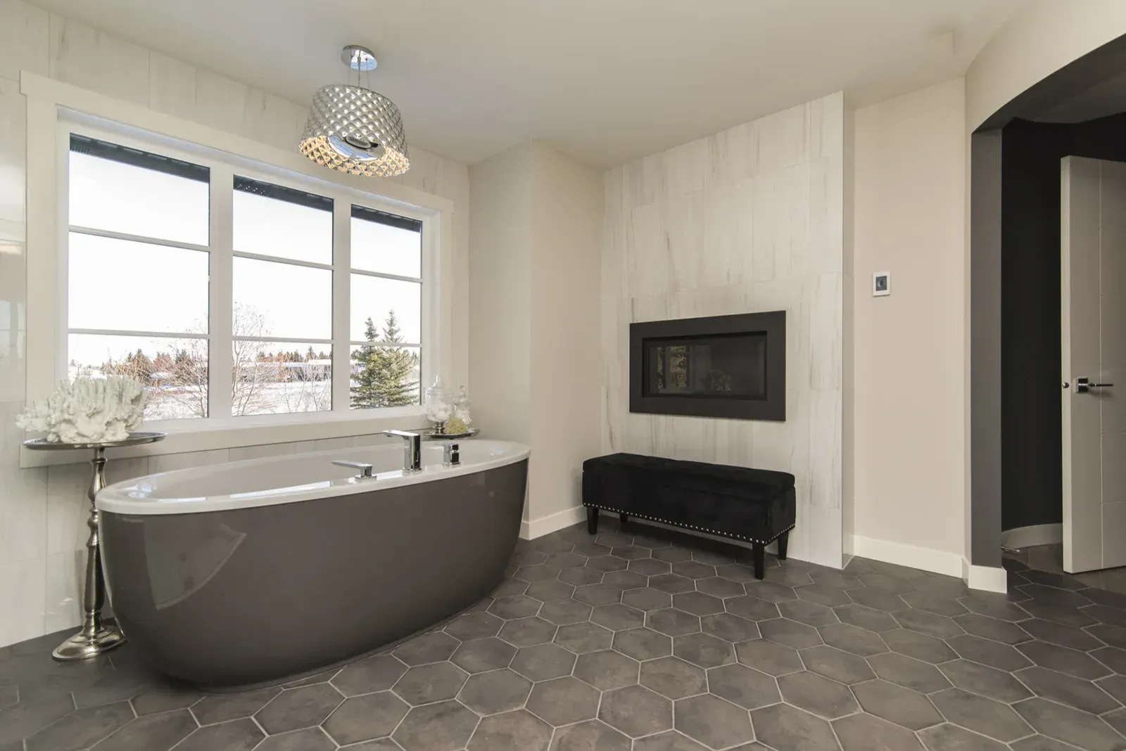 Modern bathroom with a freestanding tub, large window, black fireplace, and hexagon tile floor