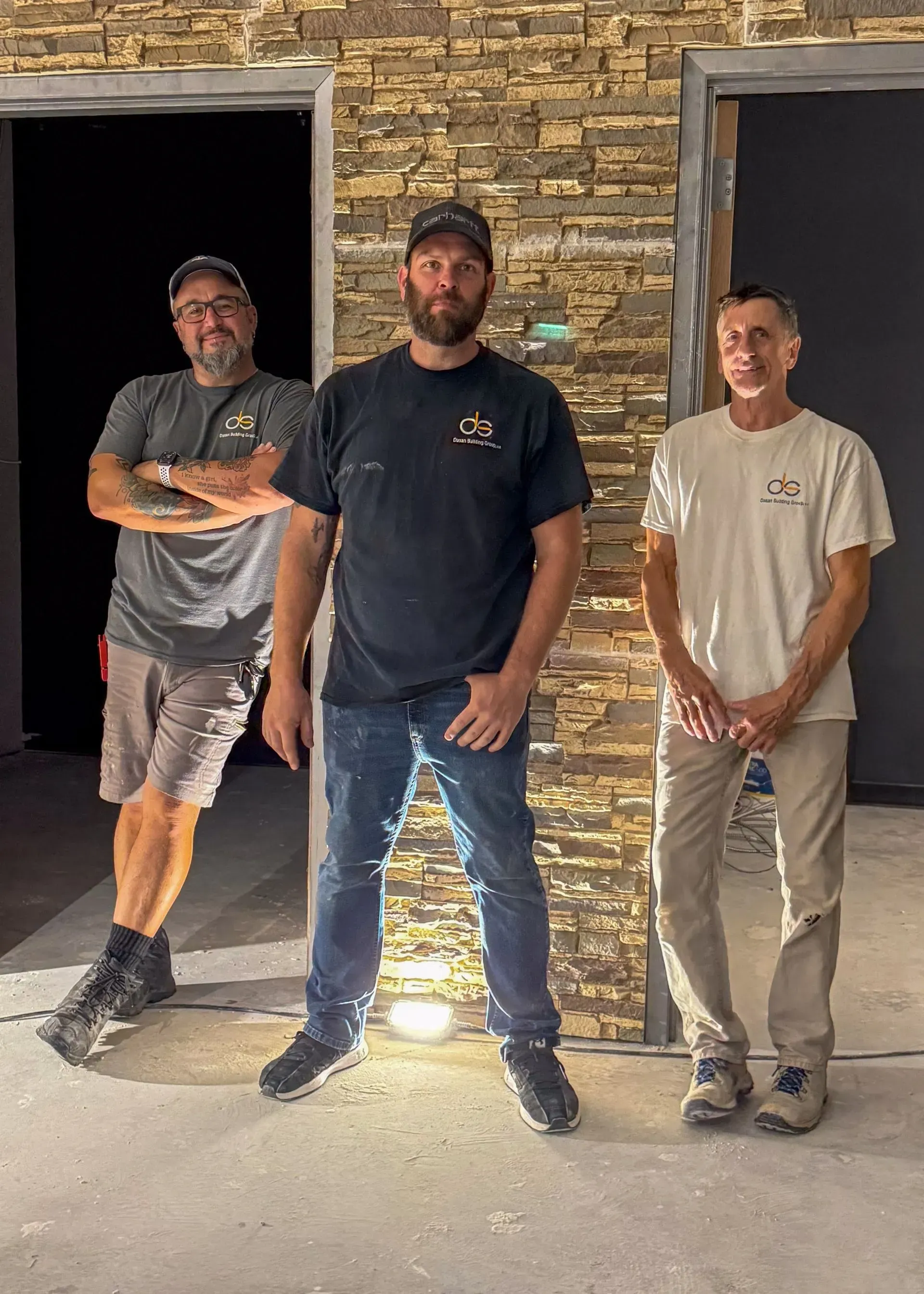 Three men standing in doorways, next to stone wall, under construction.