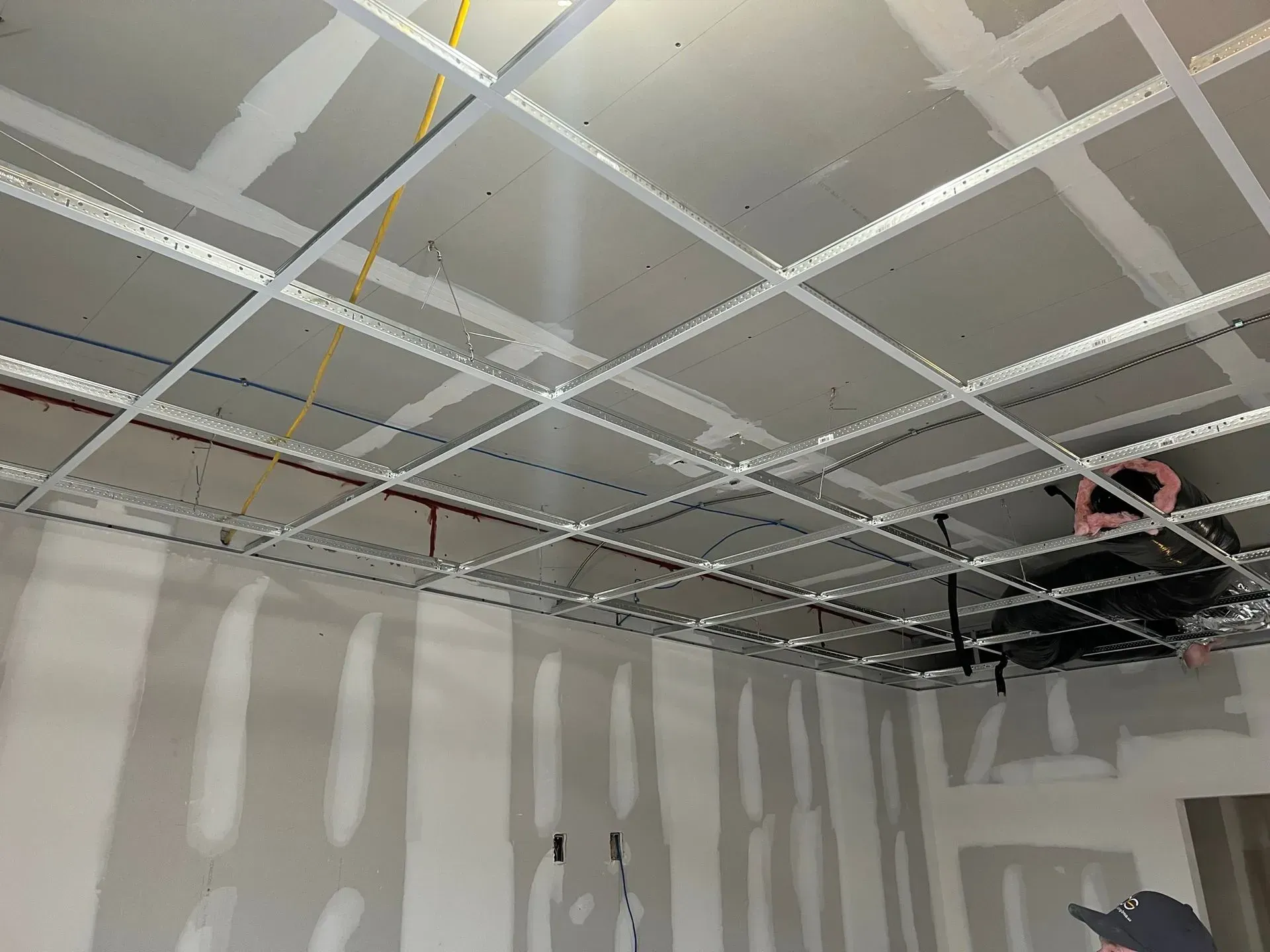 Interior room construction with drywall walls, ceiling grid, and exposed electrical wires.
