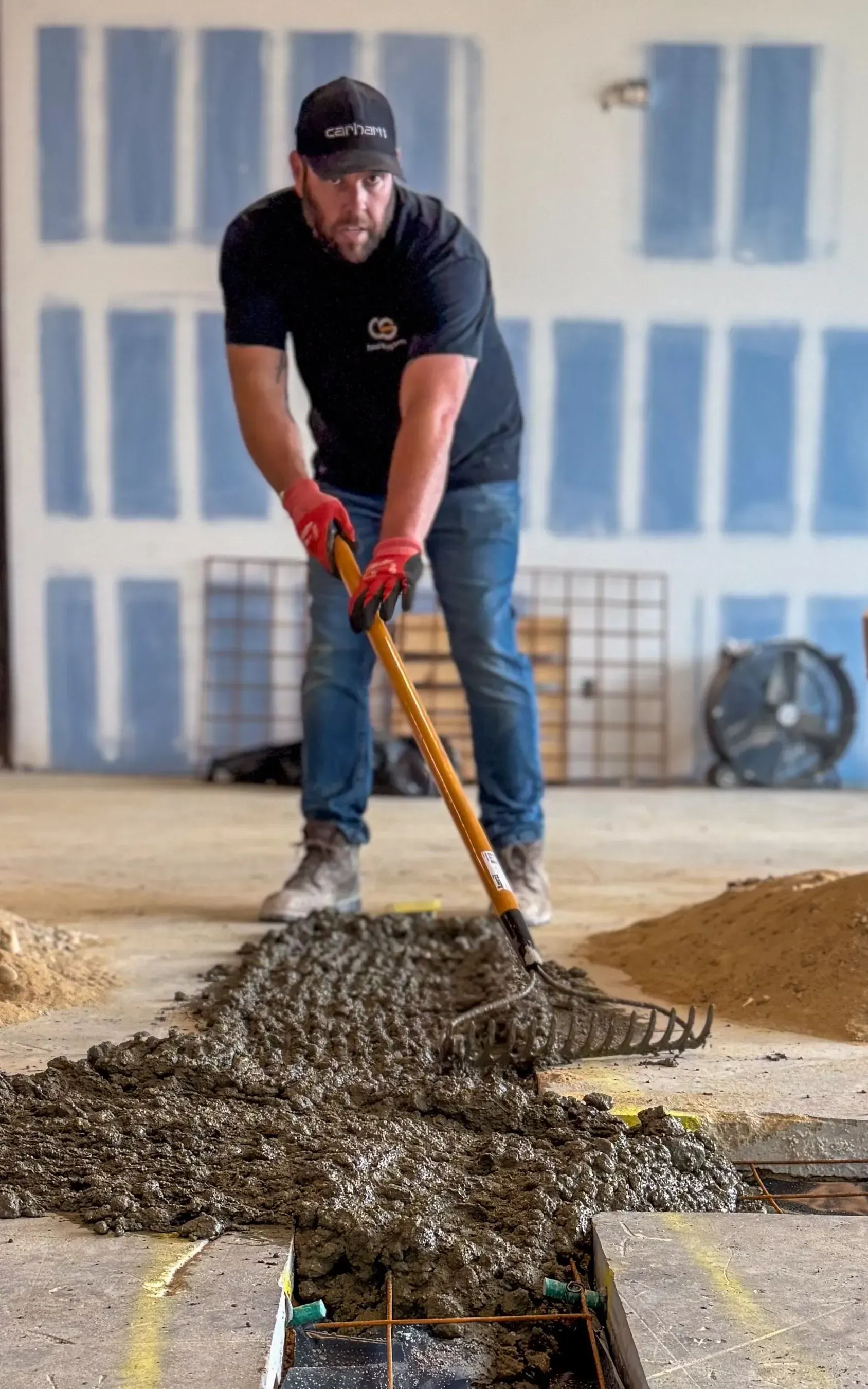 Man in black shirt uses a rake on fresh concrete in a construction area.