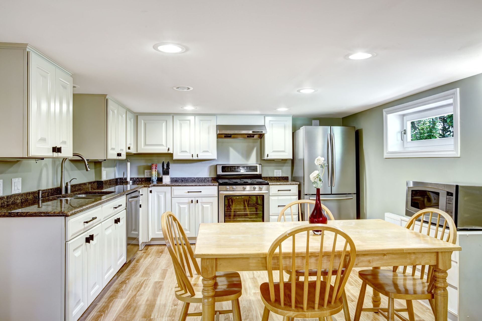 Kitchen with white cabinets, stainless steel appliances, and a wooden table with chairs.