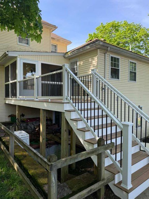 Stilted house with a white-railed staircase leading to an upper deck beside a beige siding wall.