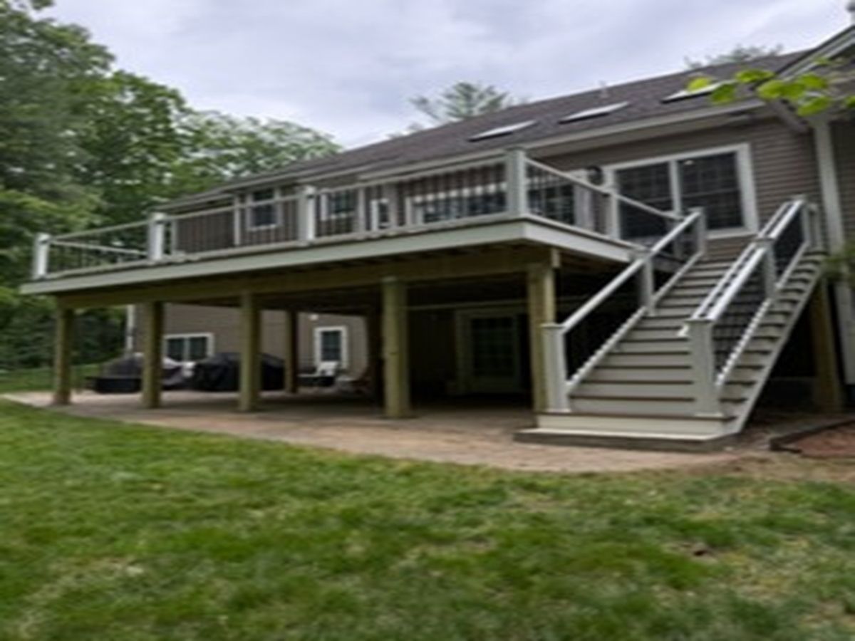 Two-story house with a raised deck, stairs, and covered patio in a grassy yard