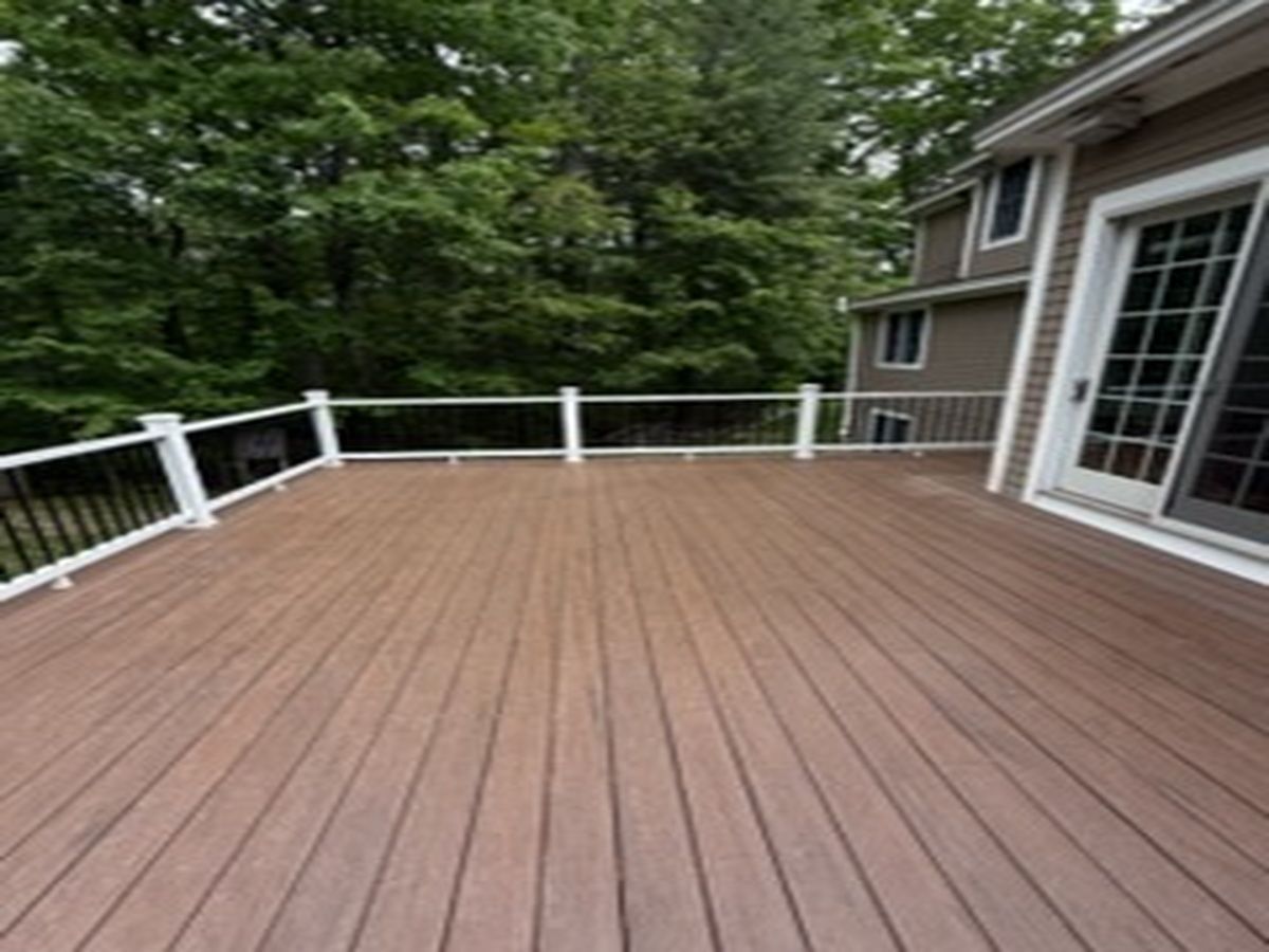 Large wooden deck with white railing beside a house and trees