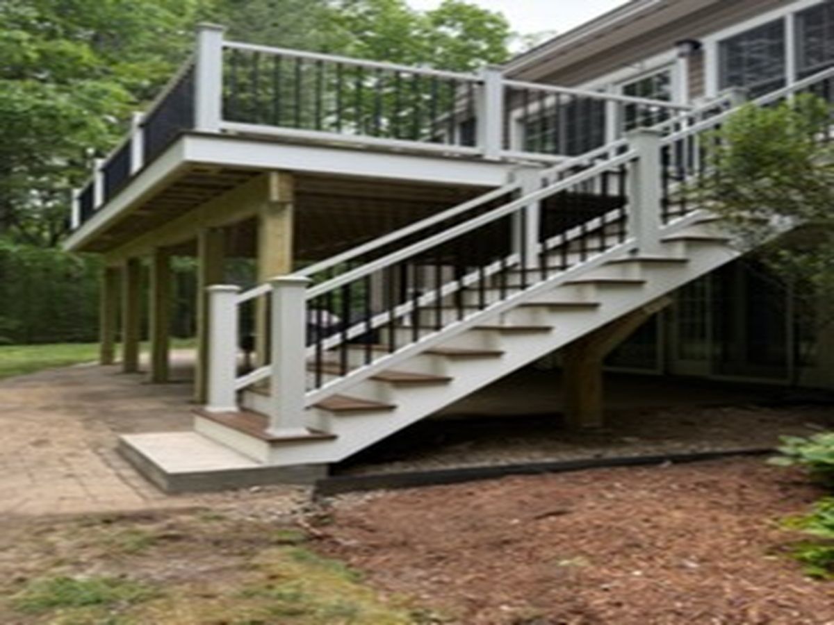 Raised deck with white stairs and black railings on wooden posts in a wooded yard