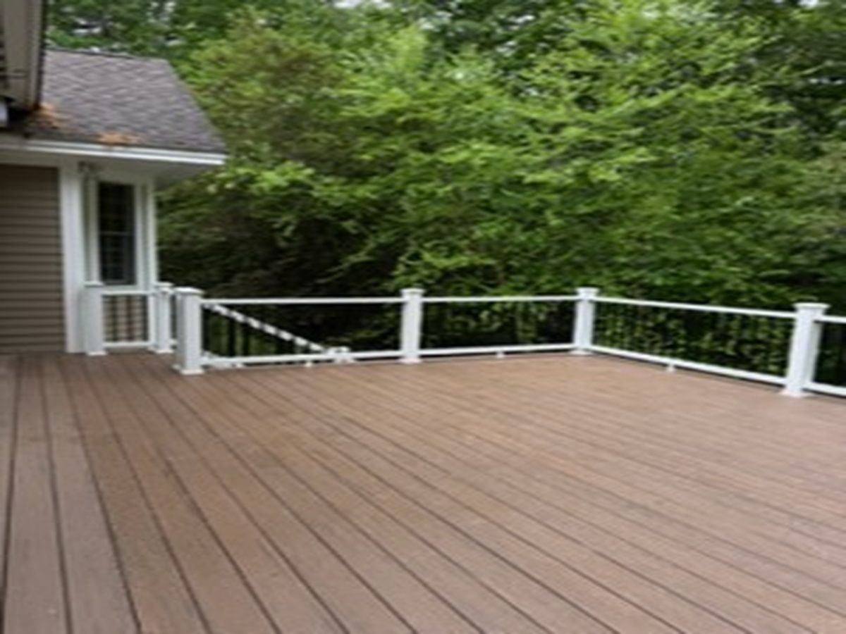 Wooden deck beside a house, with white railing and green trees in the background.