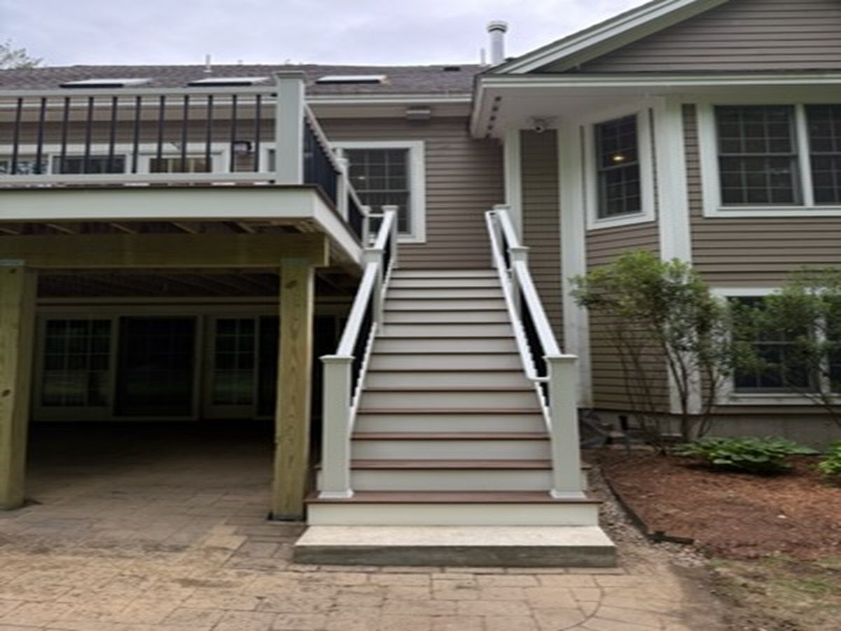Exterior staircase with white railings leading to a raised entryway beside a carport.
